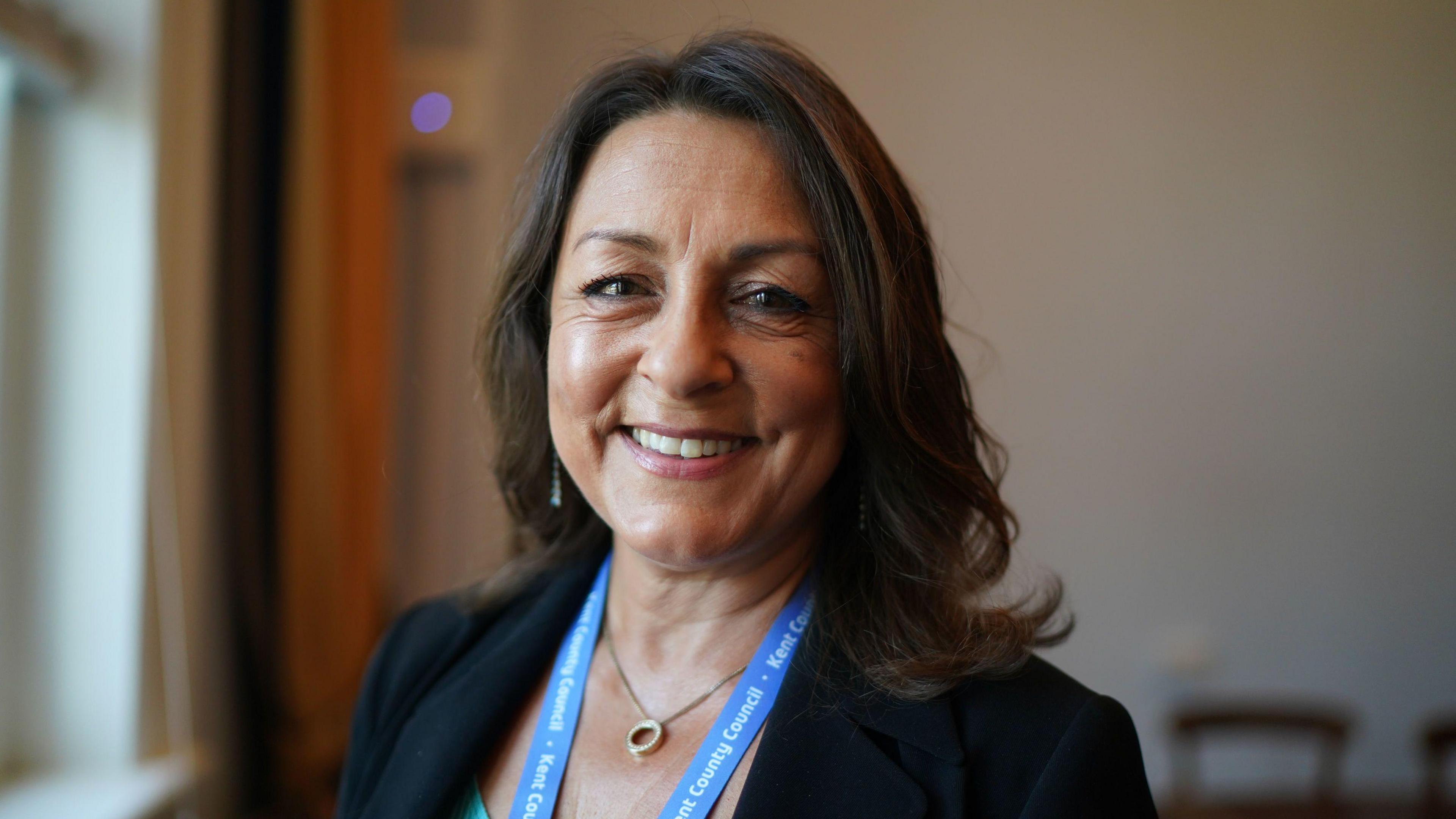 Linden Kemkaran wears a turquoise top under a dark jacket and looks directly into the camera, smiling.
