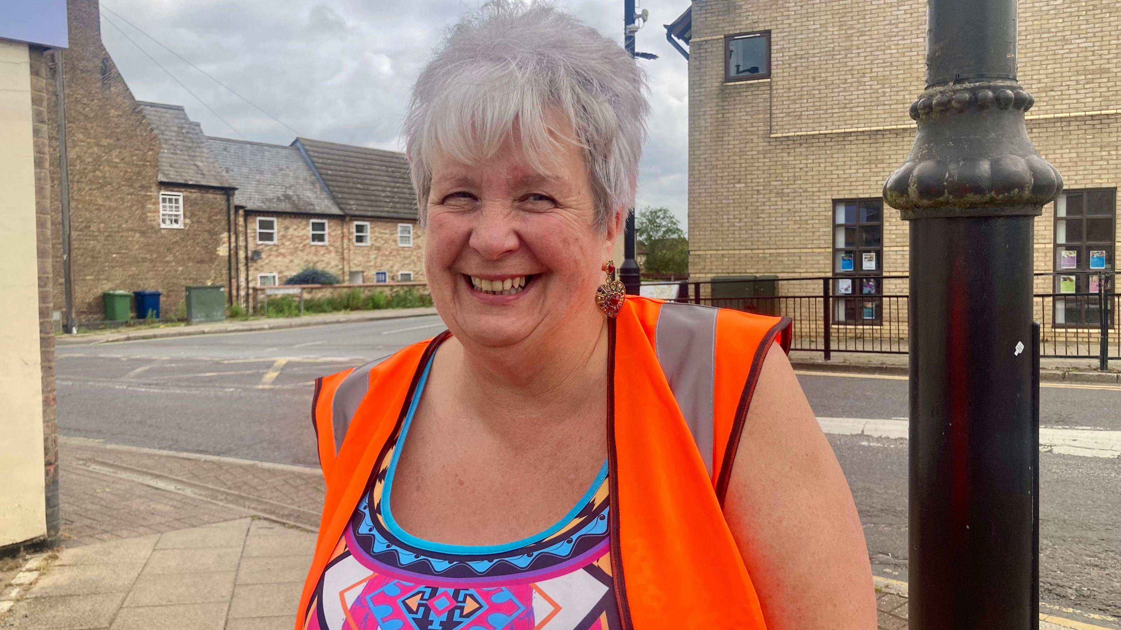 Sue Unwin smiling while standing at the base of a lamppost in the town.