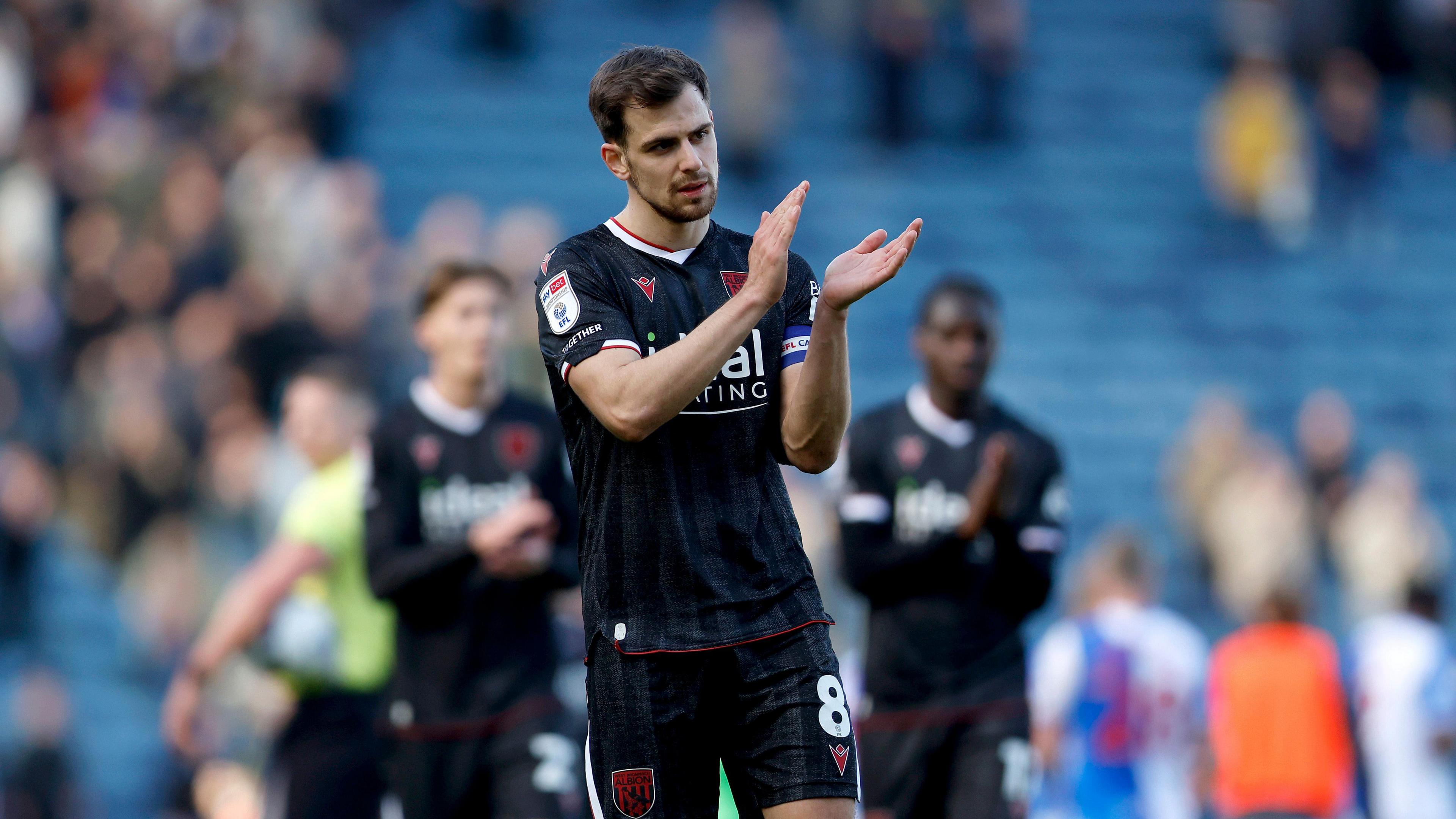 A photo of Jayson Molumby applauding fans in West Bromwich Albion's black and red third kit