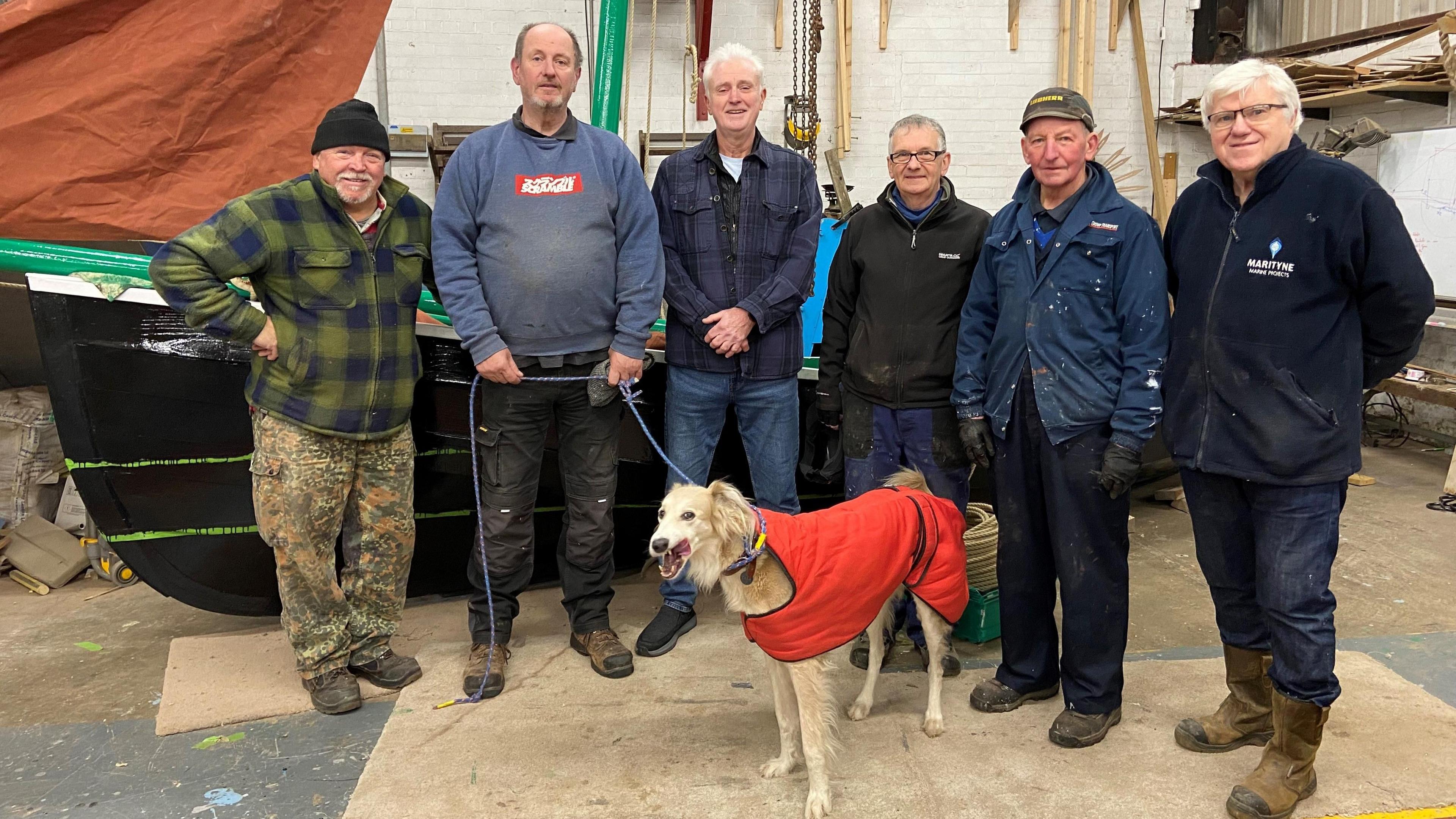 Trustees Peter Johnson, Martin Wilson, Jim Sullivan, Peter Aitken, Alex Sheriff and George McCann at the workshop. Mr Wilson is holding a dog, called Cara, on a lead.
