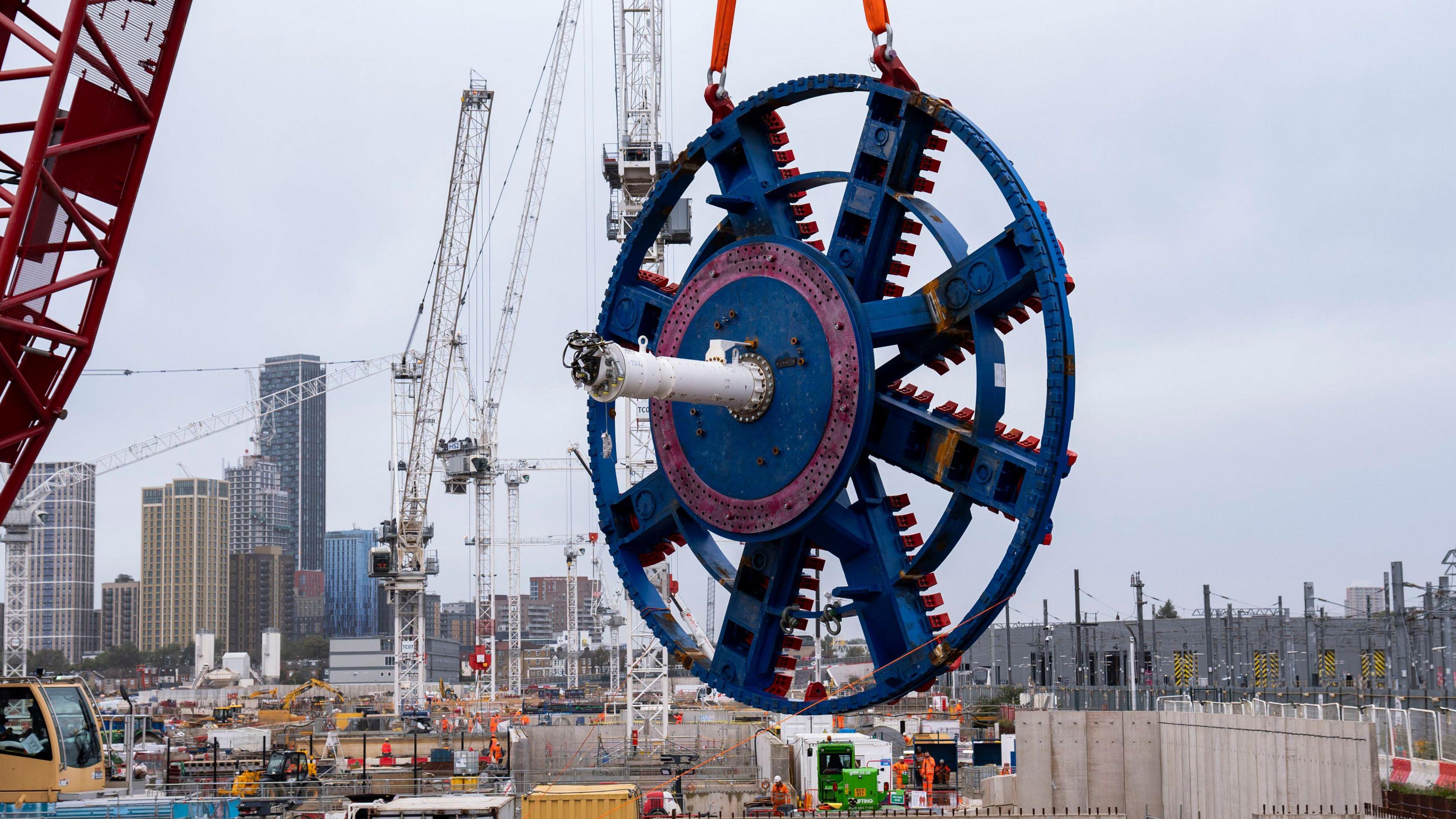 A red crane lifts a giant blue and red steel 'cutterhead' from one of the Euston Tunnel boring machines at the HS2 site on Atlas Road in Old Oak Common