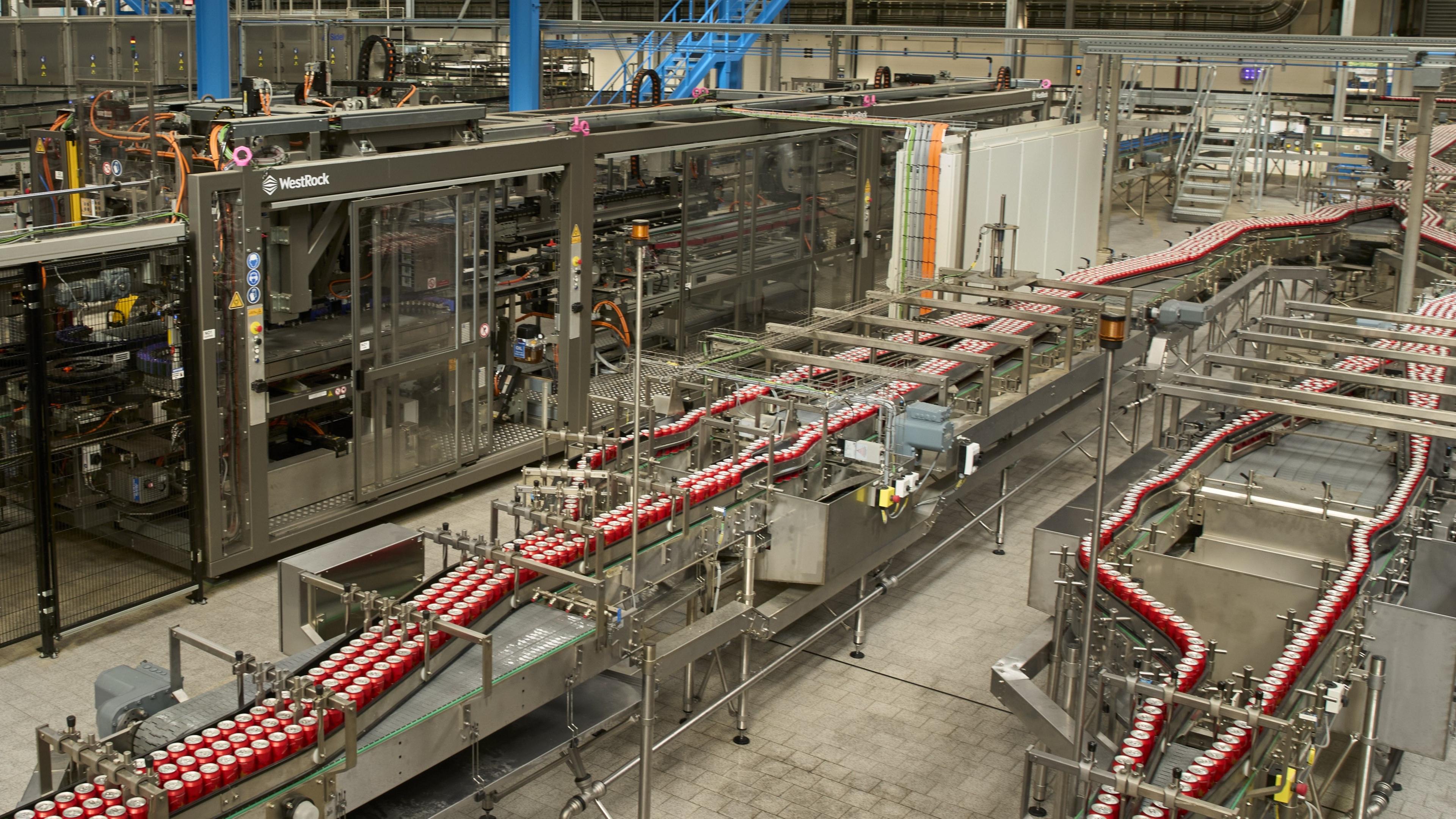 The production line of a brewery with lots of red cans on canning lines.