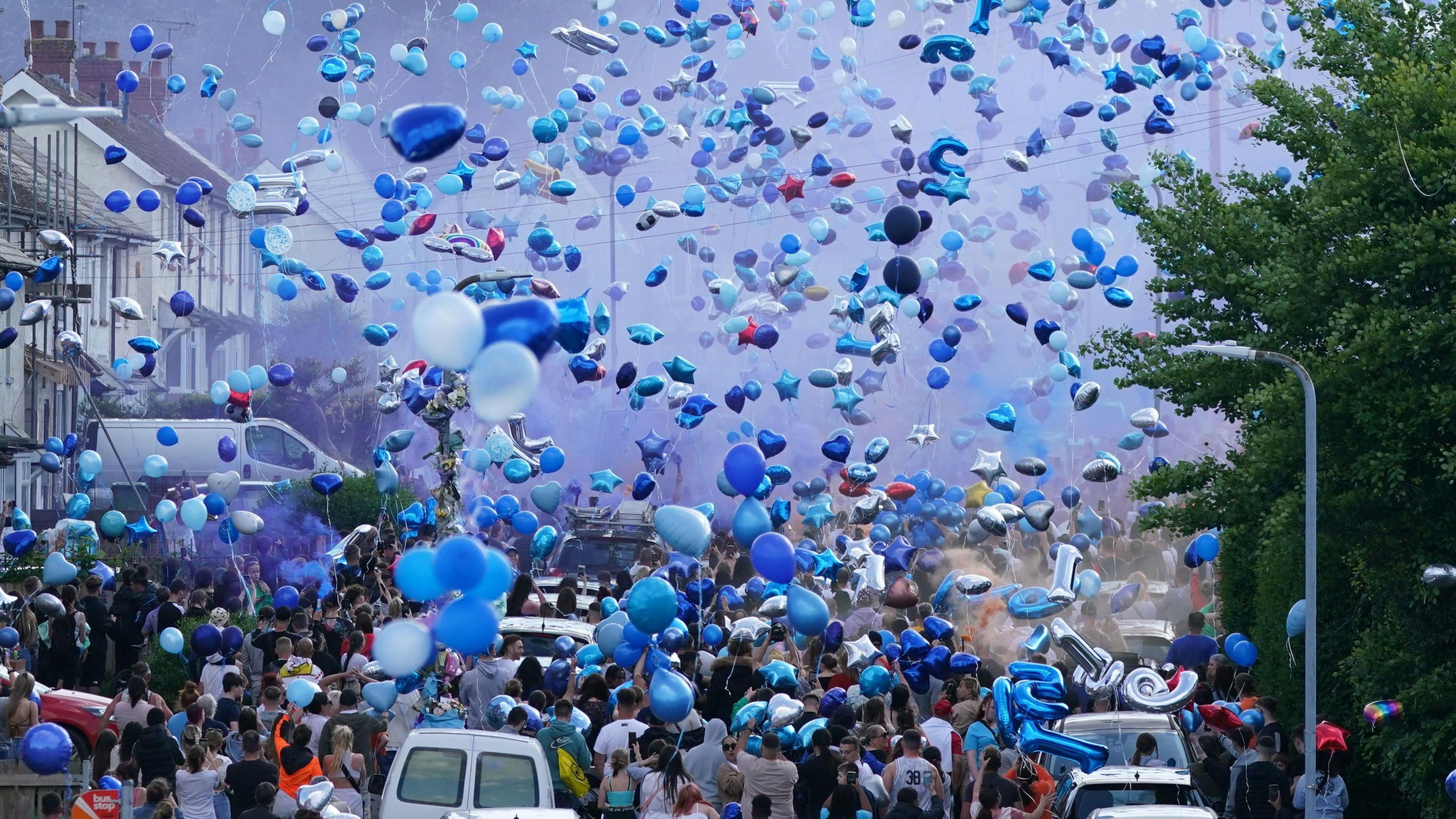 People release blue balloons in a residential street during a vigil for the victims in Ely, Cardiff.

