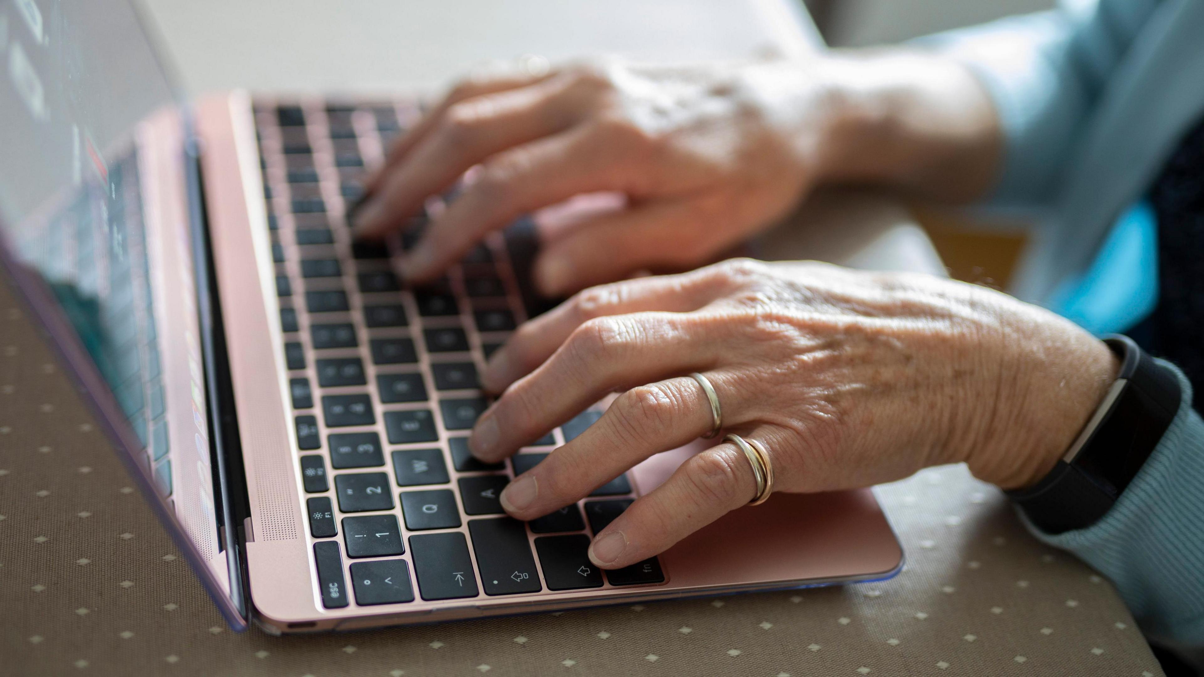 A woman's hands typing using a pink chrome laptop keyboard. 