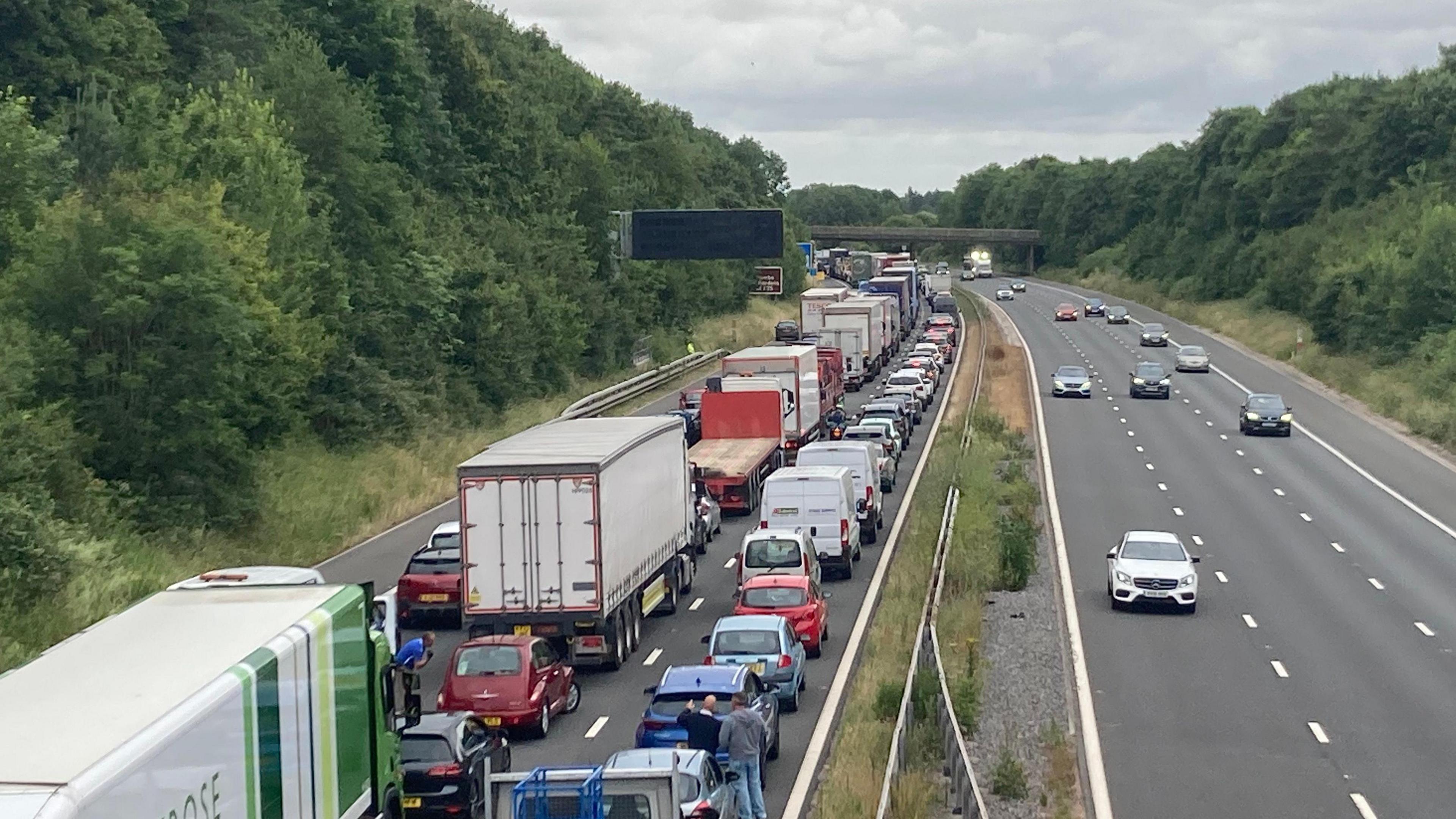 Queueing traffic including cars and lorries on the northbound side. Flowing traffic on the southbound side.