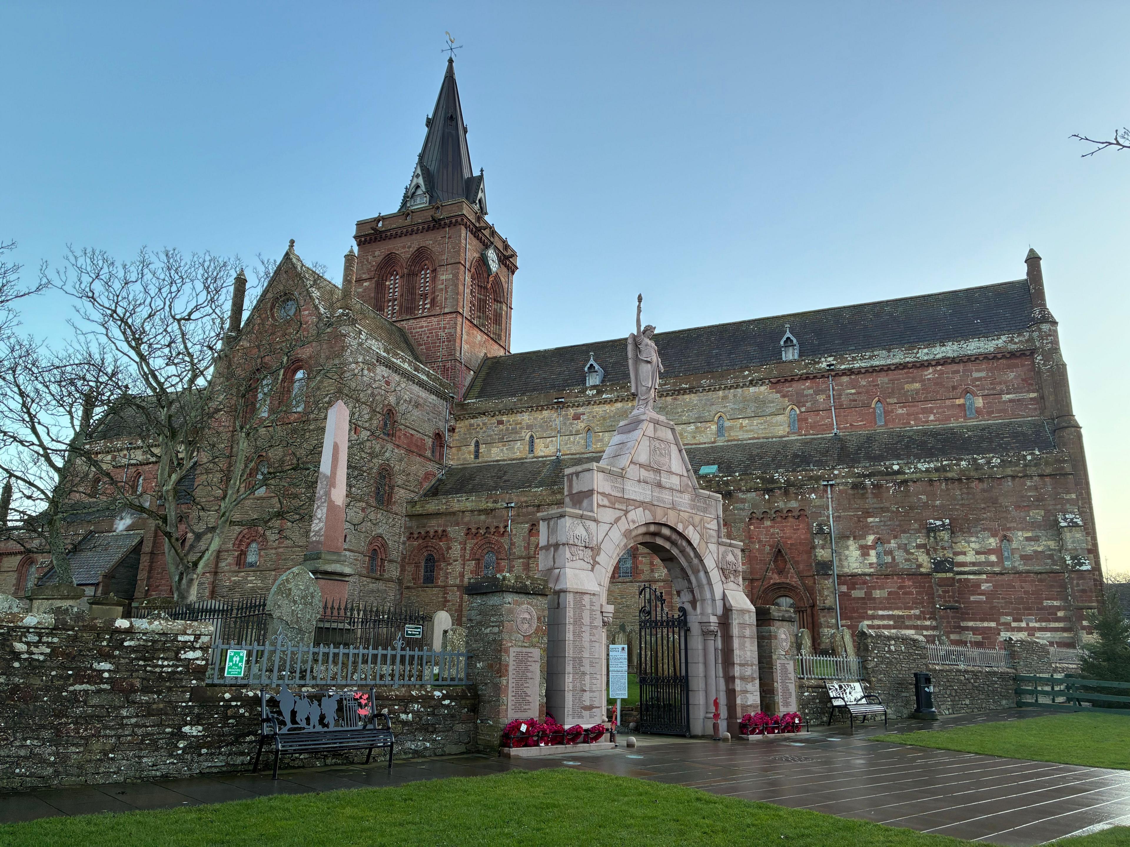The exterior of St Magnus Cathedral - an old red stone building with a steeple. 