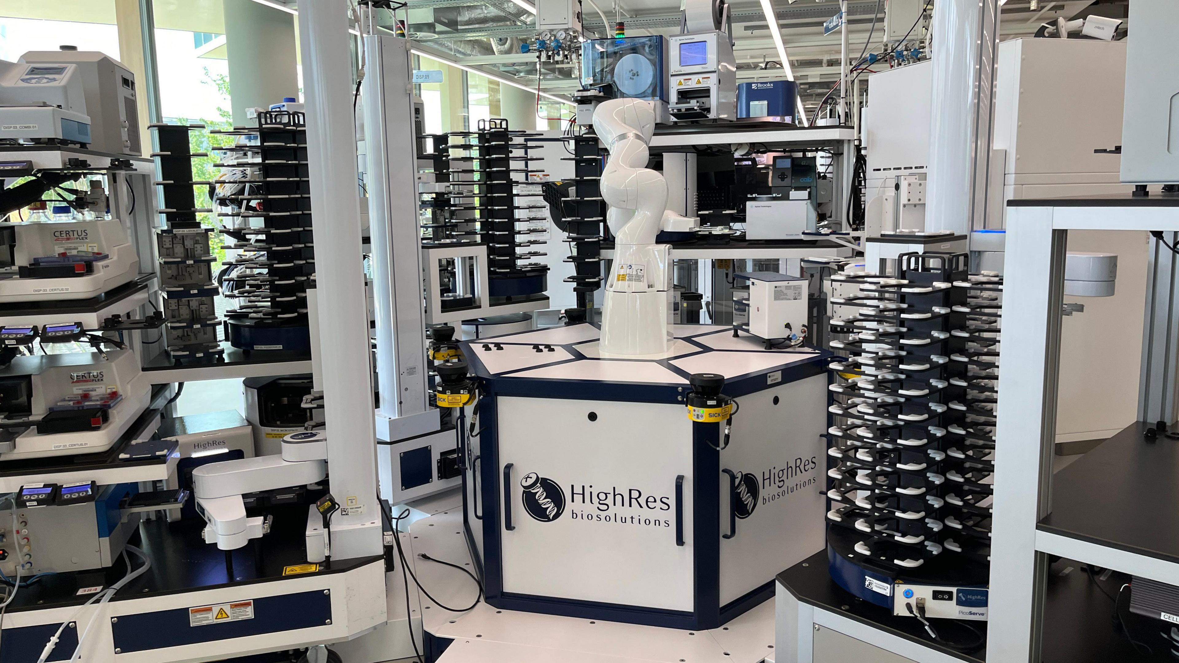 An interior shot of a white robotic arm, surrounded by other scientific equipment. On the base of the arm is written "high res biosolutions". 