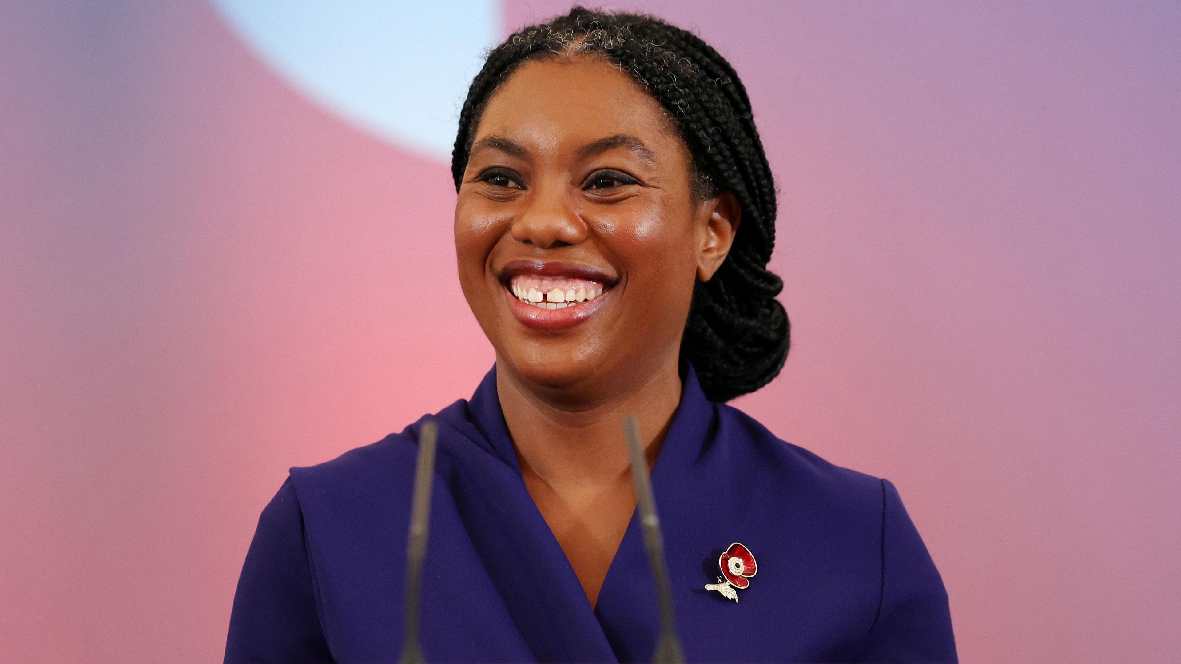 Kemi Badenoch smiles on stage wearing a blue blazer to deliver her victory speech 