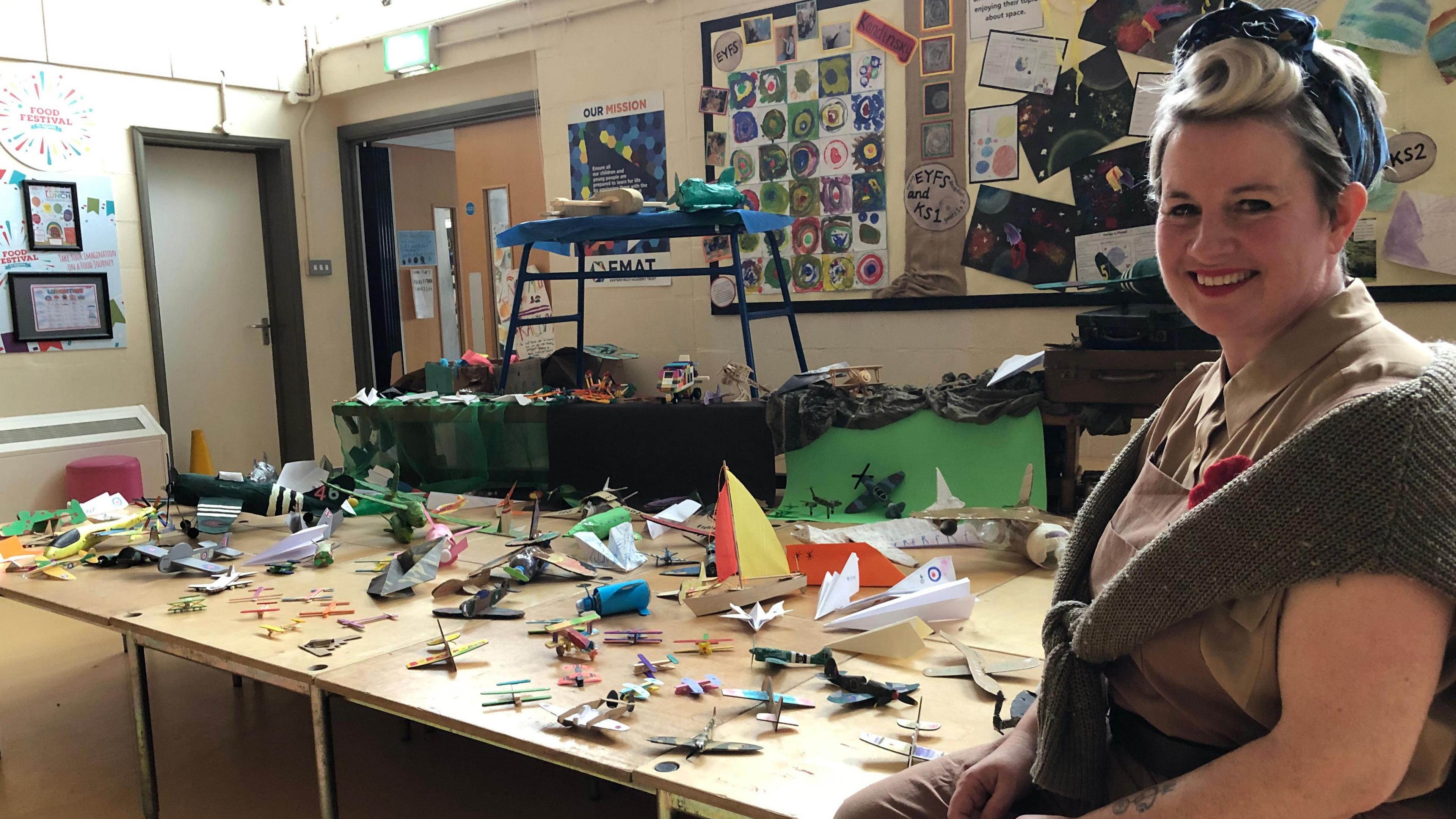 Head of Art at Nelson Academy Jill Sek dressed as a member of the Women's Land Army sitting in front of D-Day planes and boats made by the children. 