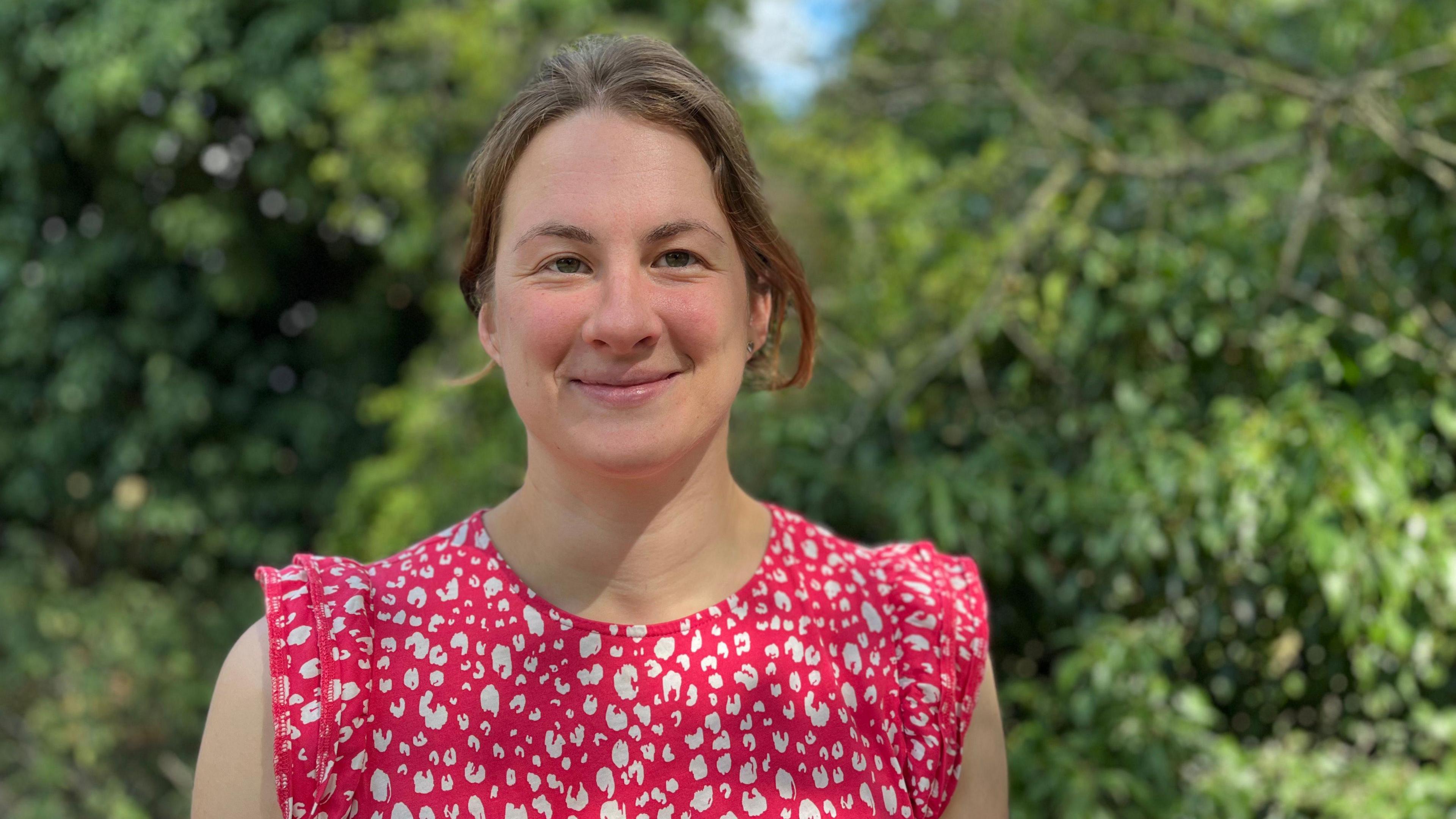 Rosie smiles at the camera. She has light brown hair and wears a pink and white patterned top.