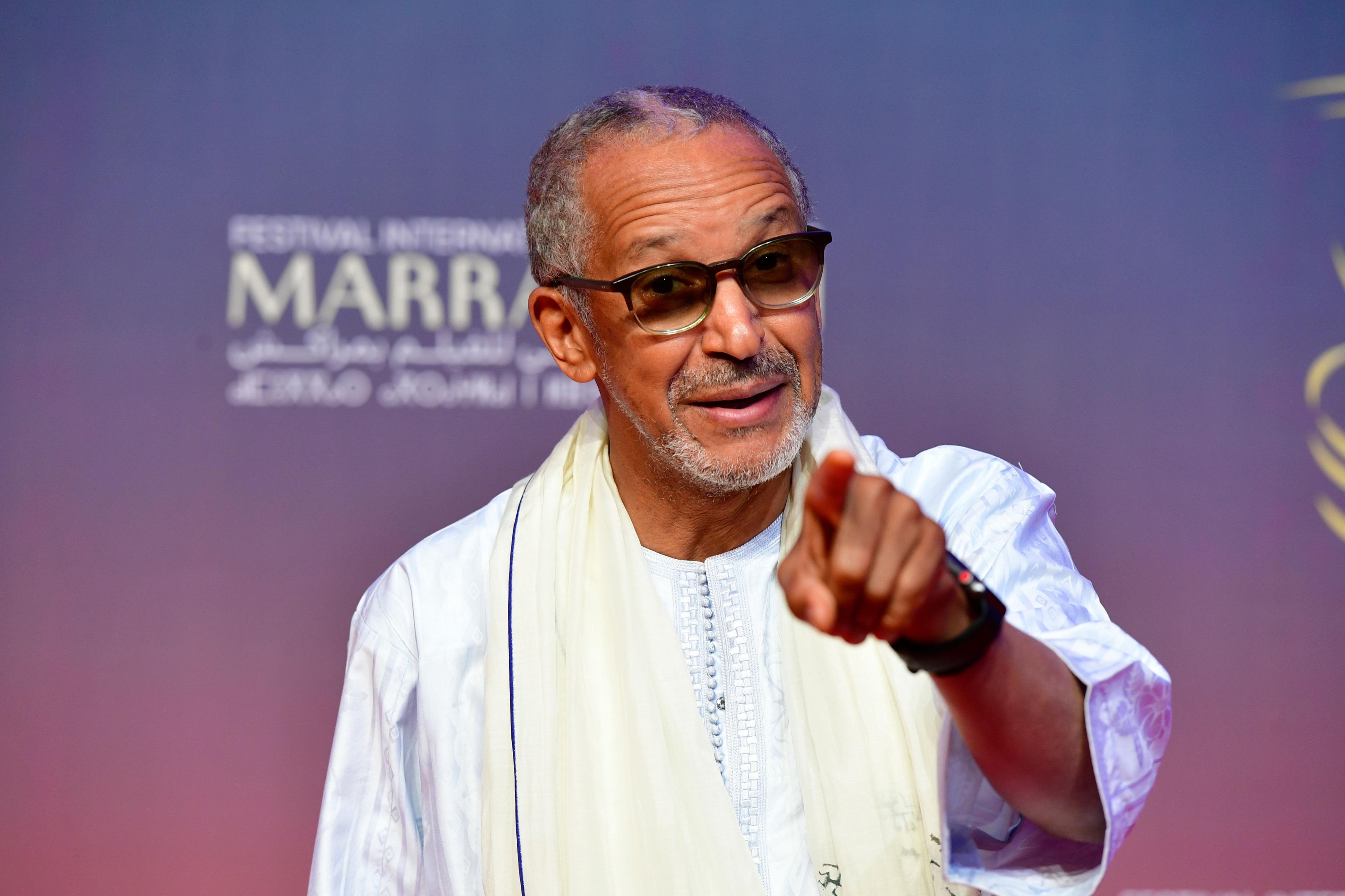 Abderrahmane Sissako wearing tinted glasses and a boubou points at the camera in a jocular way in Marrakesh - Saturday 7 December 2024