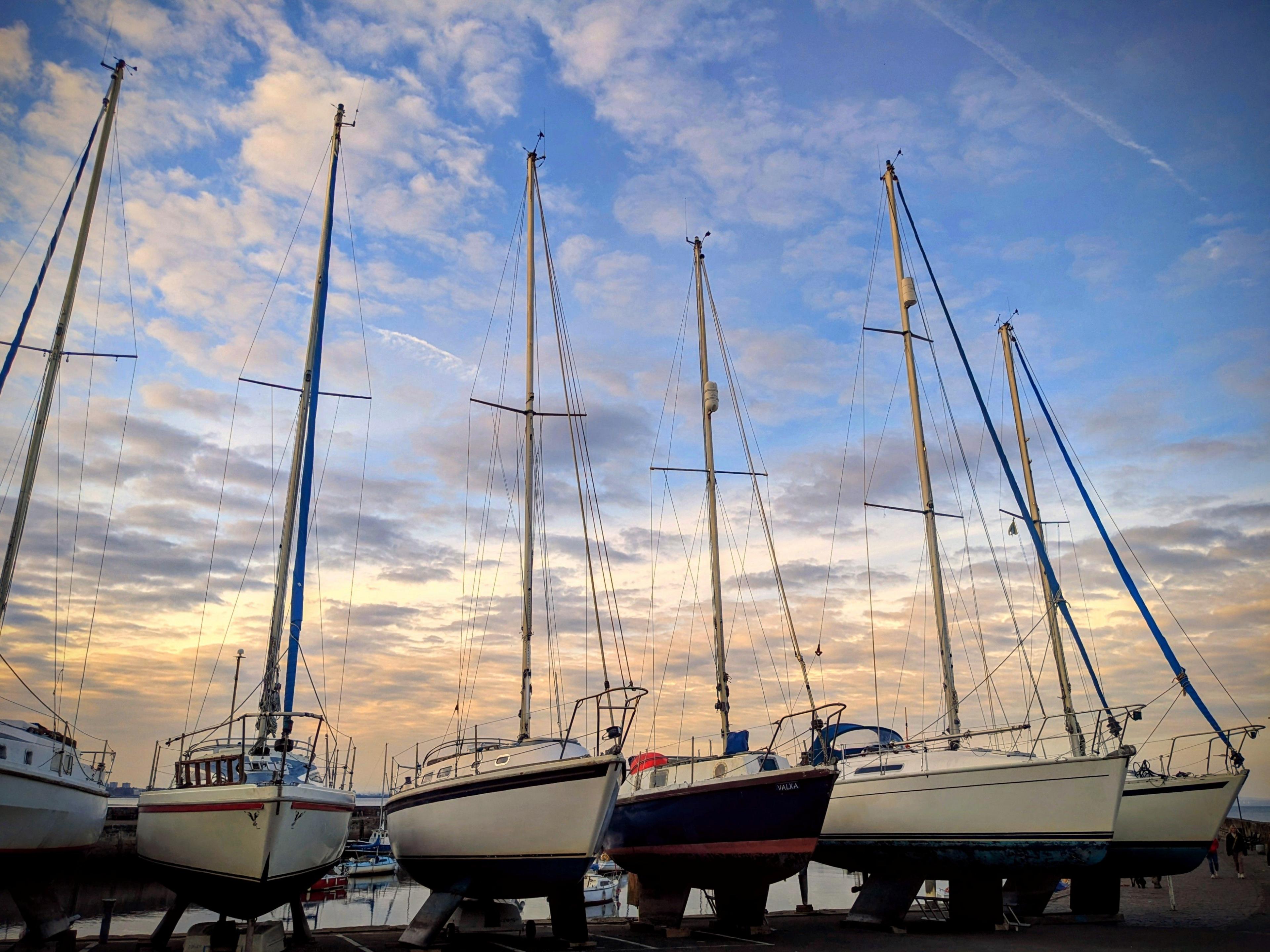 Six boats lined up next to each other in a harbour, on a sunny day with blue skies above them.