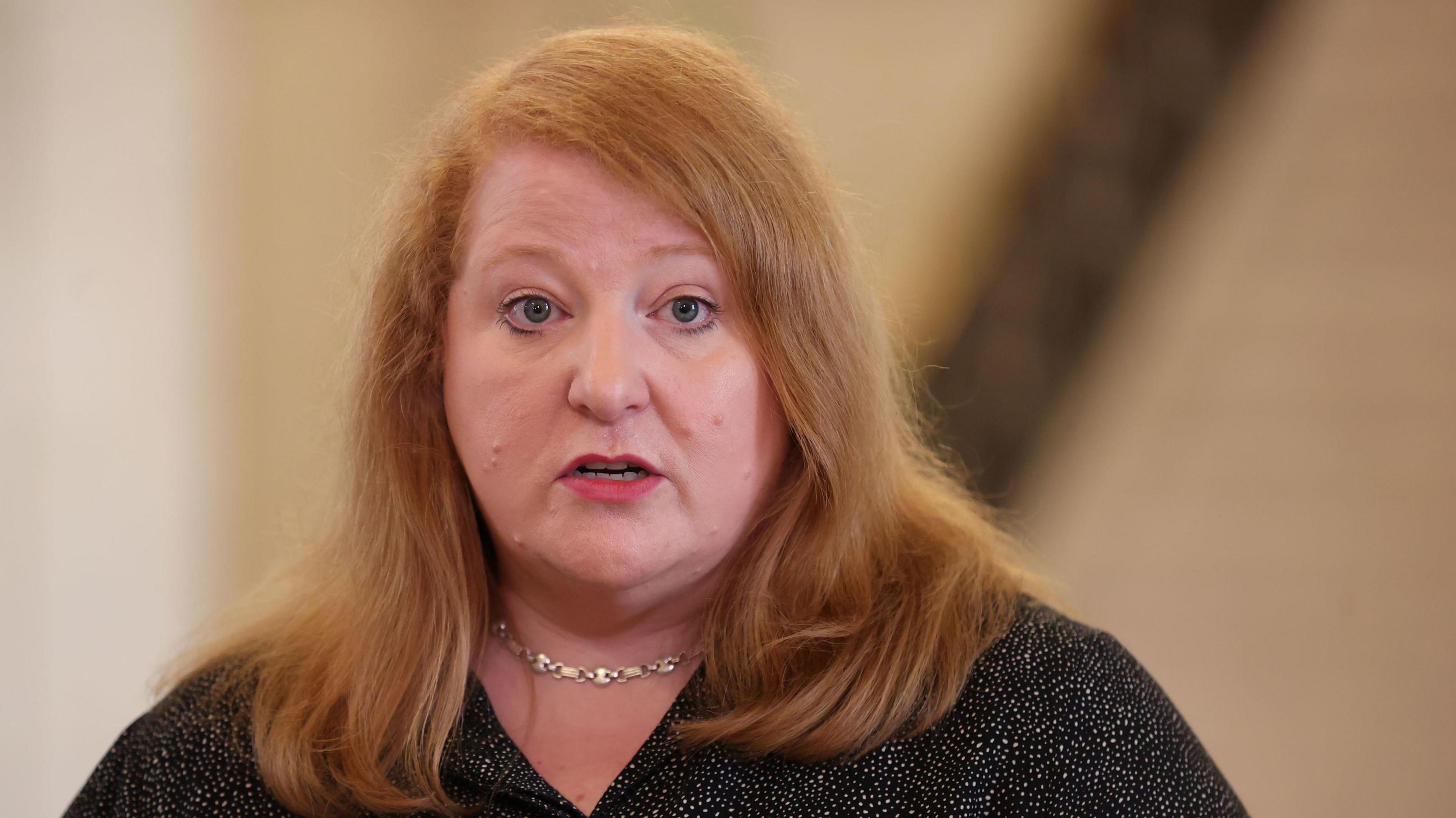 Naomi  Long. She has shoulder-length strawberry blonde hair, wearing a black blouse and silver necklace.