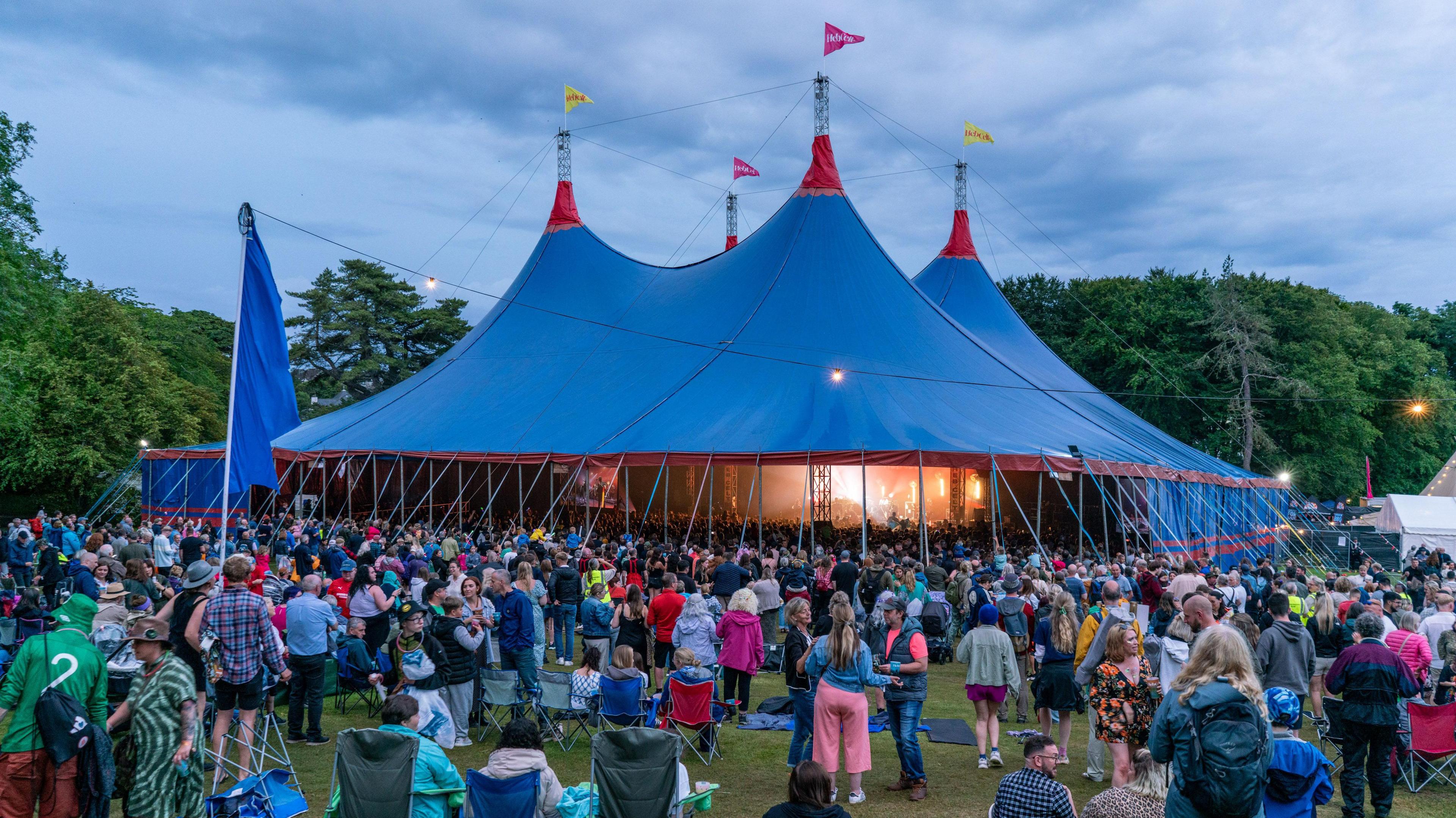 Tent aig fèis-chiùil le làn dhaoine air a taobh a-muigh.