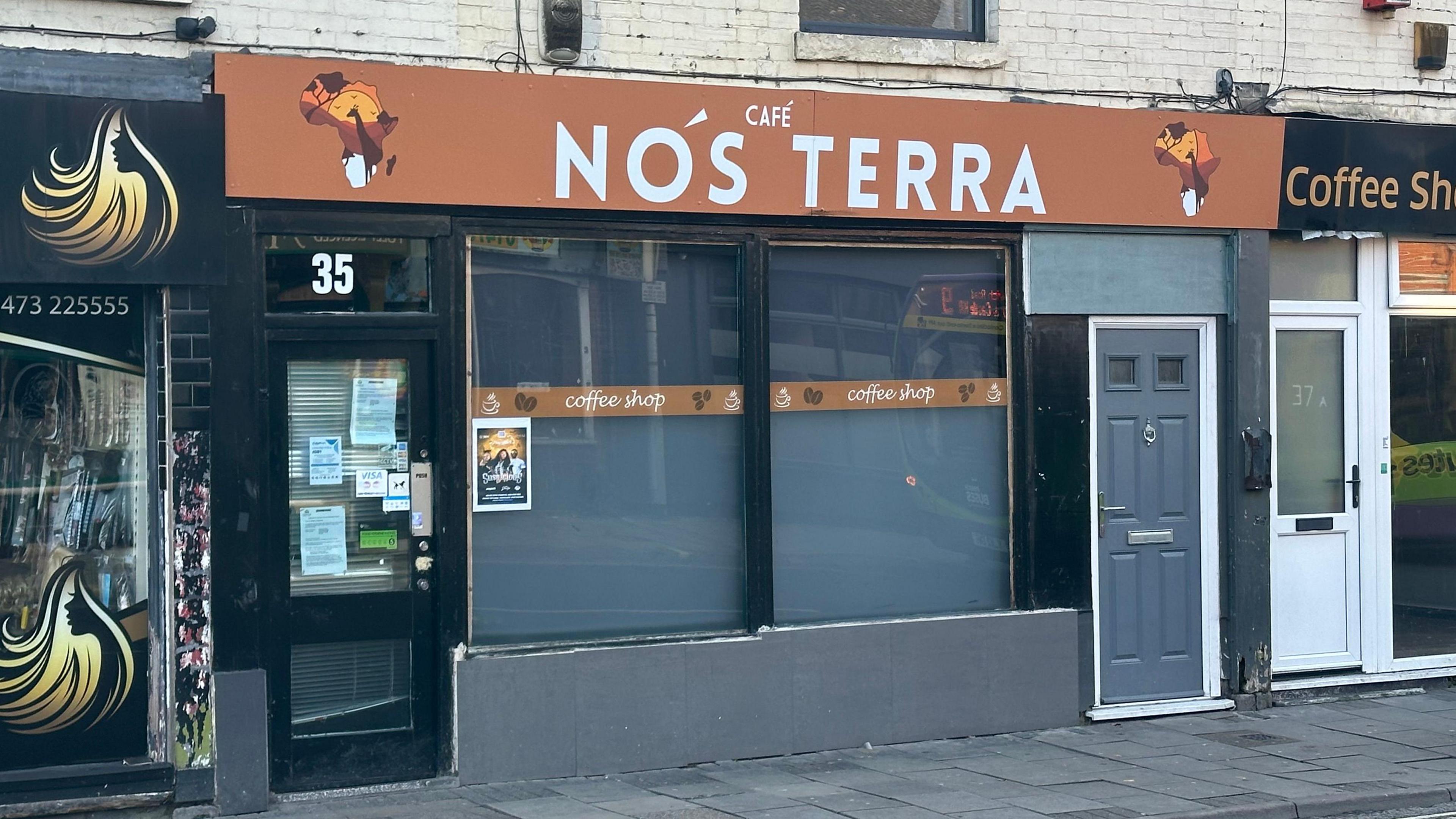 The frontage of Cafe Nos Terra in Ipswich. Its sign at the top of the building is orange with white writing.