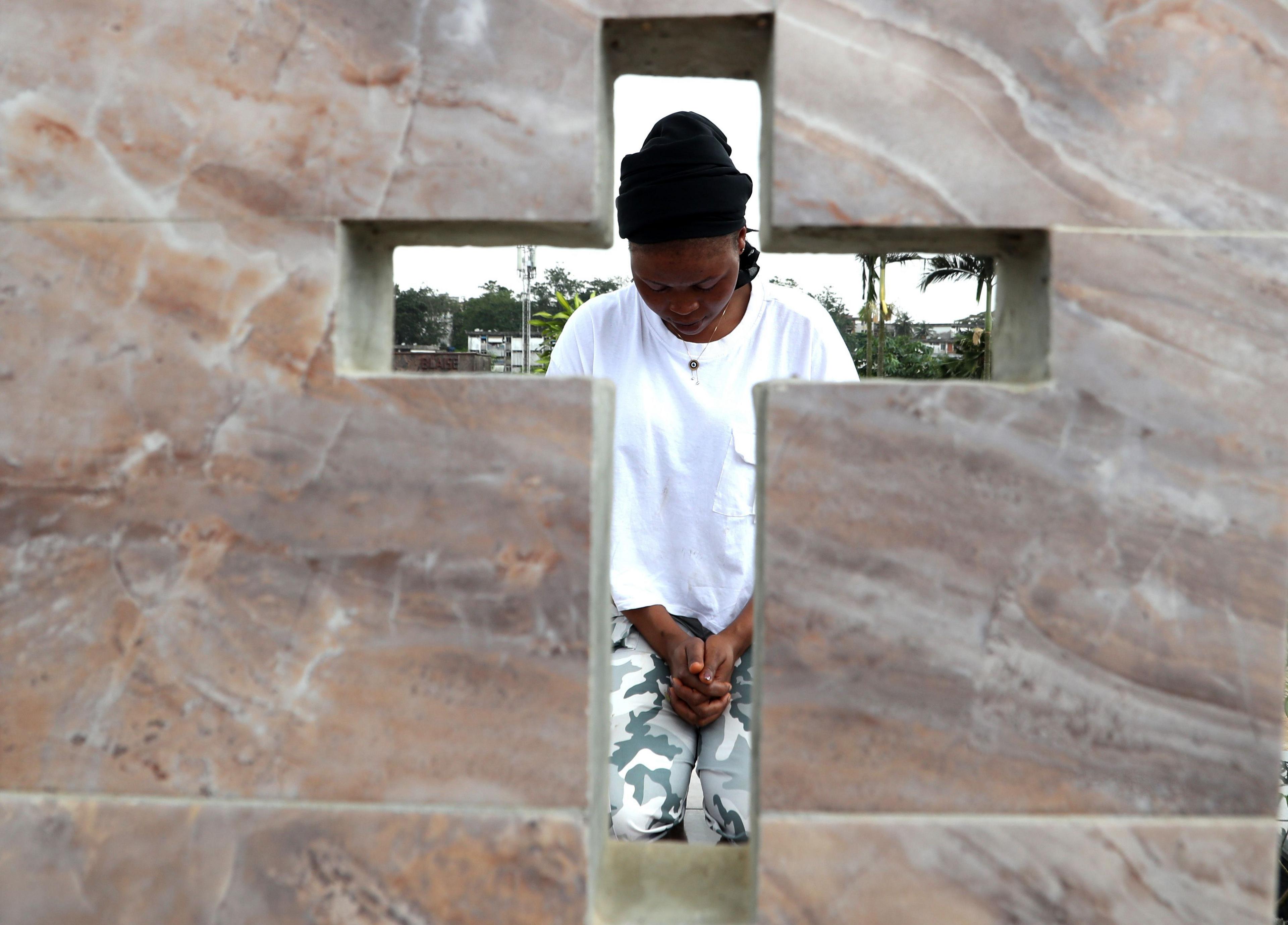 A woman is seen throw the cross of gravestone as she bows her head and clasps her hands in Abidjan, Ivory Coast - Friday 1 November 2024