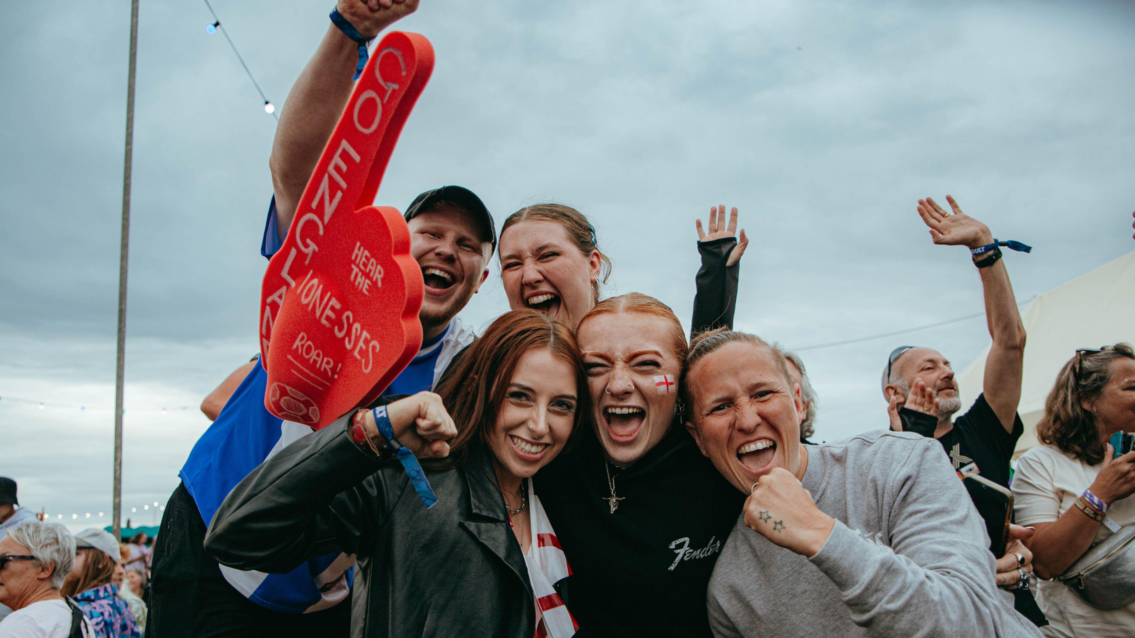 A group of people at Truck Festival punching the air as the Lionesses win Euro 2025. Some of them have face paintings of the England flag.