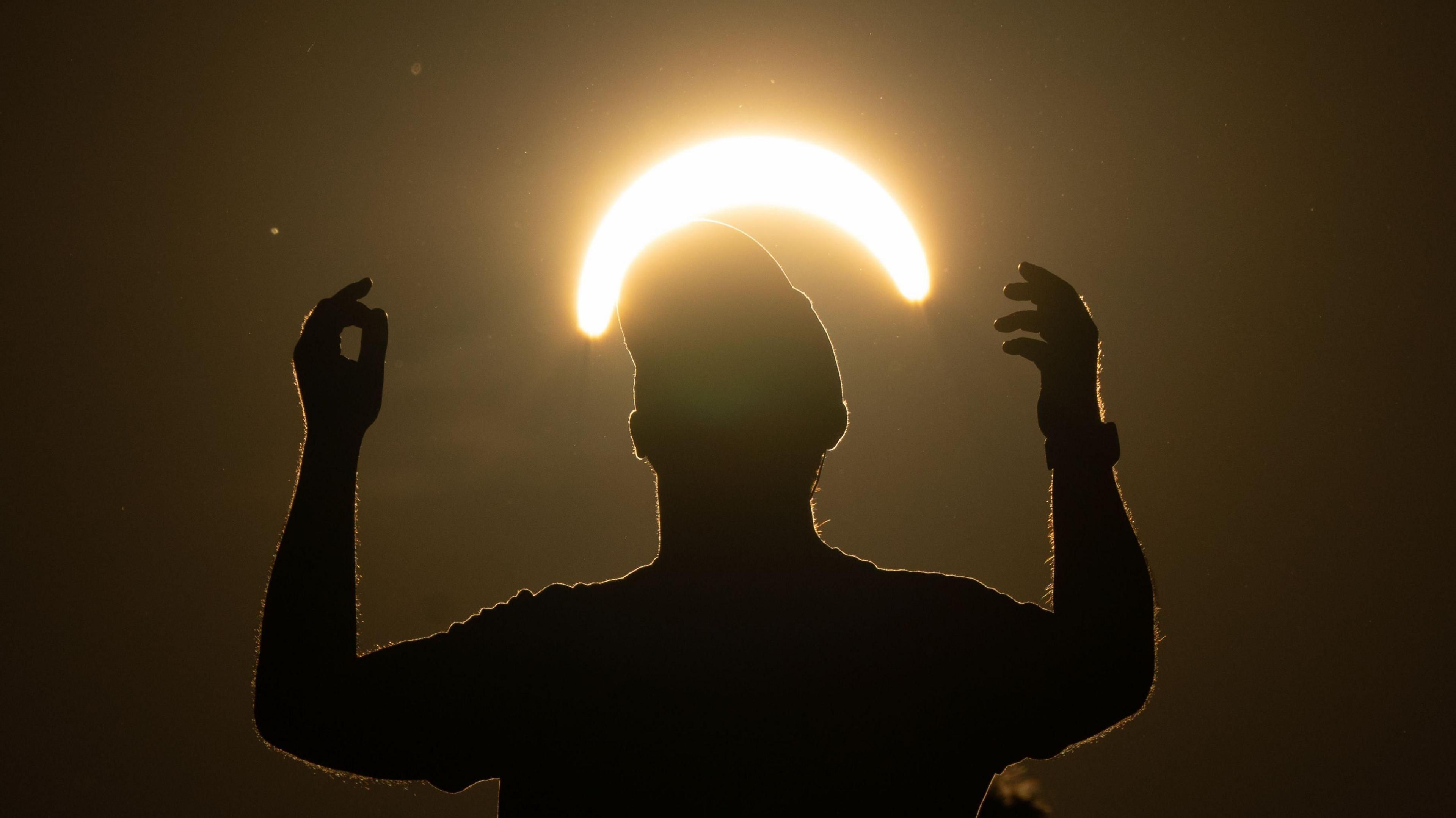 A man wearing a cap dances beneath a partial solar eclipse and the crescent of the Sun.