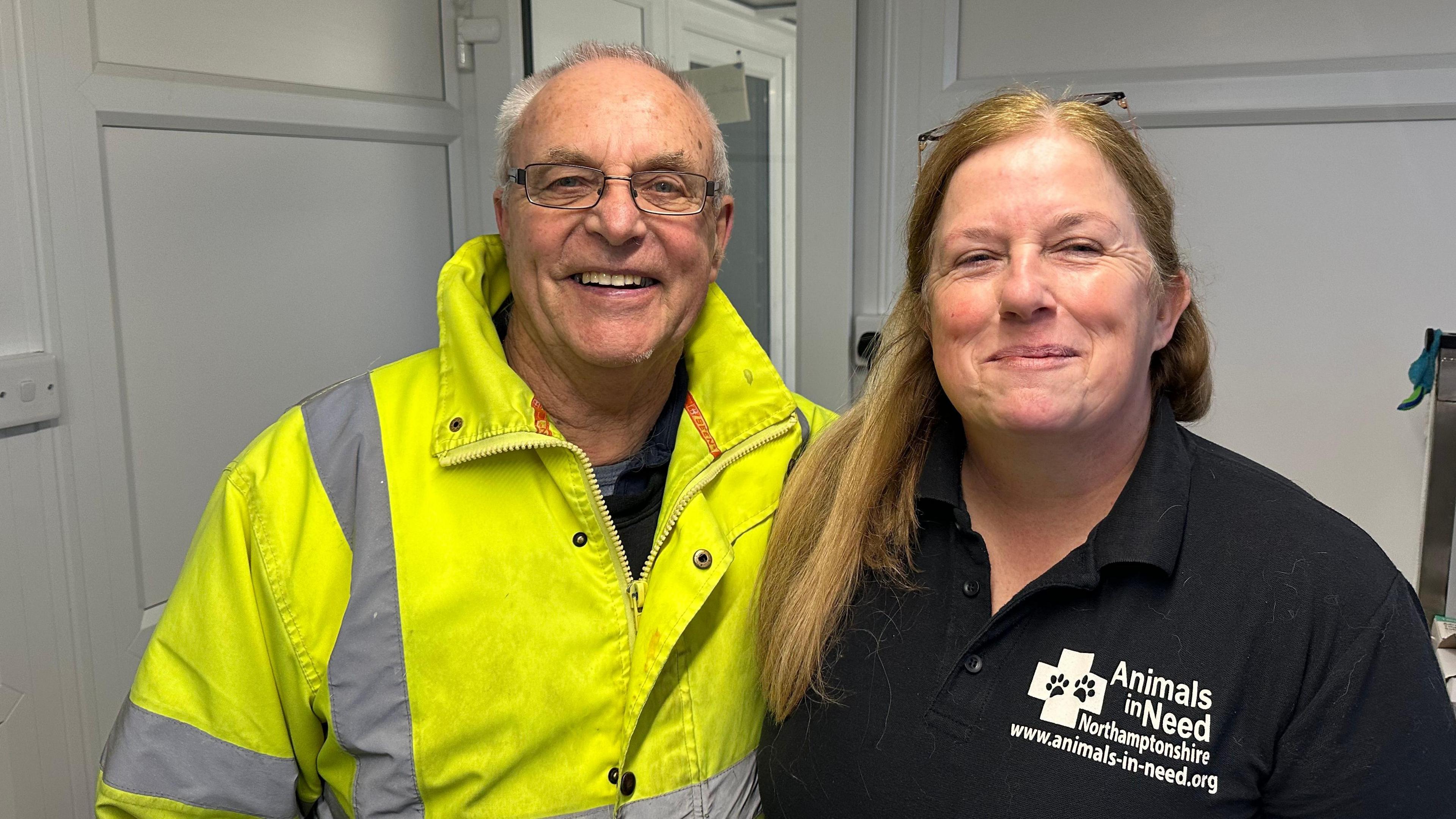 Roy Marriott and Annie Marriott smile at the camera while standing side by side. Roy wears a high-visibility coat with glasses and has his arm around Annie, who is wearing a navy polo top with strawberry blonde hair. 