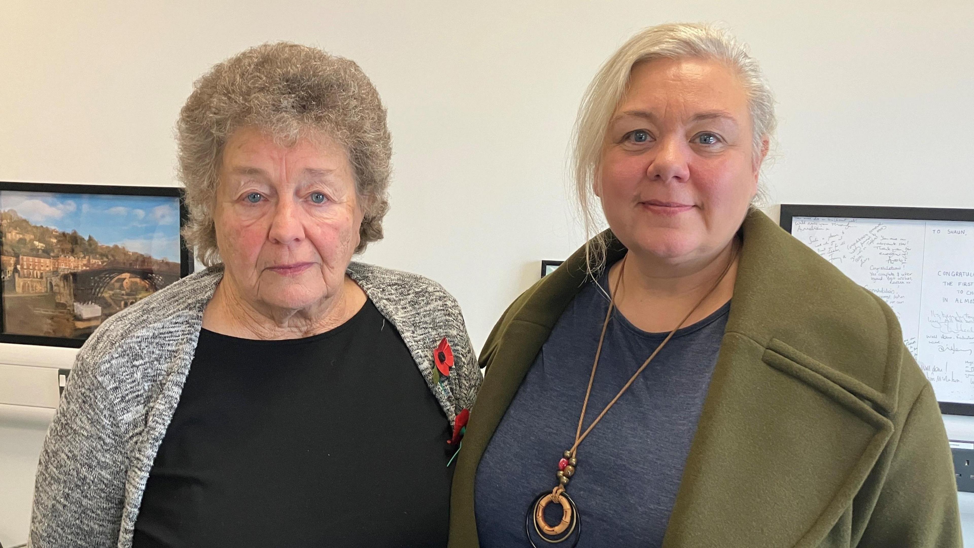 Two women, Rosemary Southgate and her niece Sarah Dukes, posing for a photo with a plain white wall behind them. Both are wearing poppies.