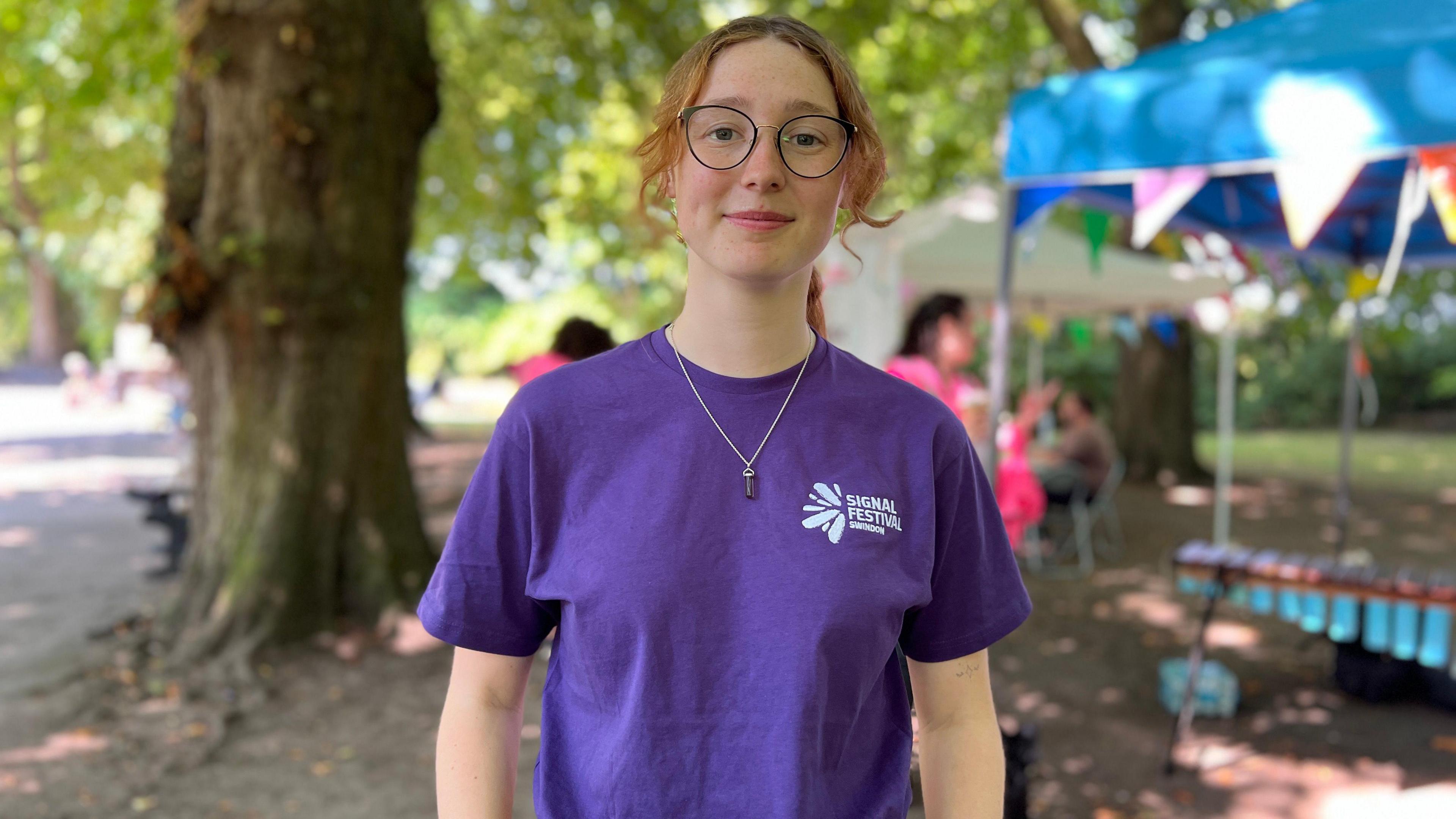 A girl wearing a purple t-shirt looks into the camera