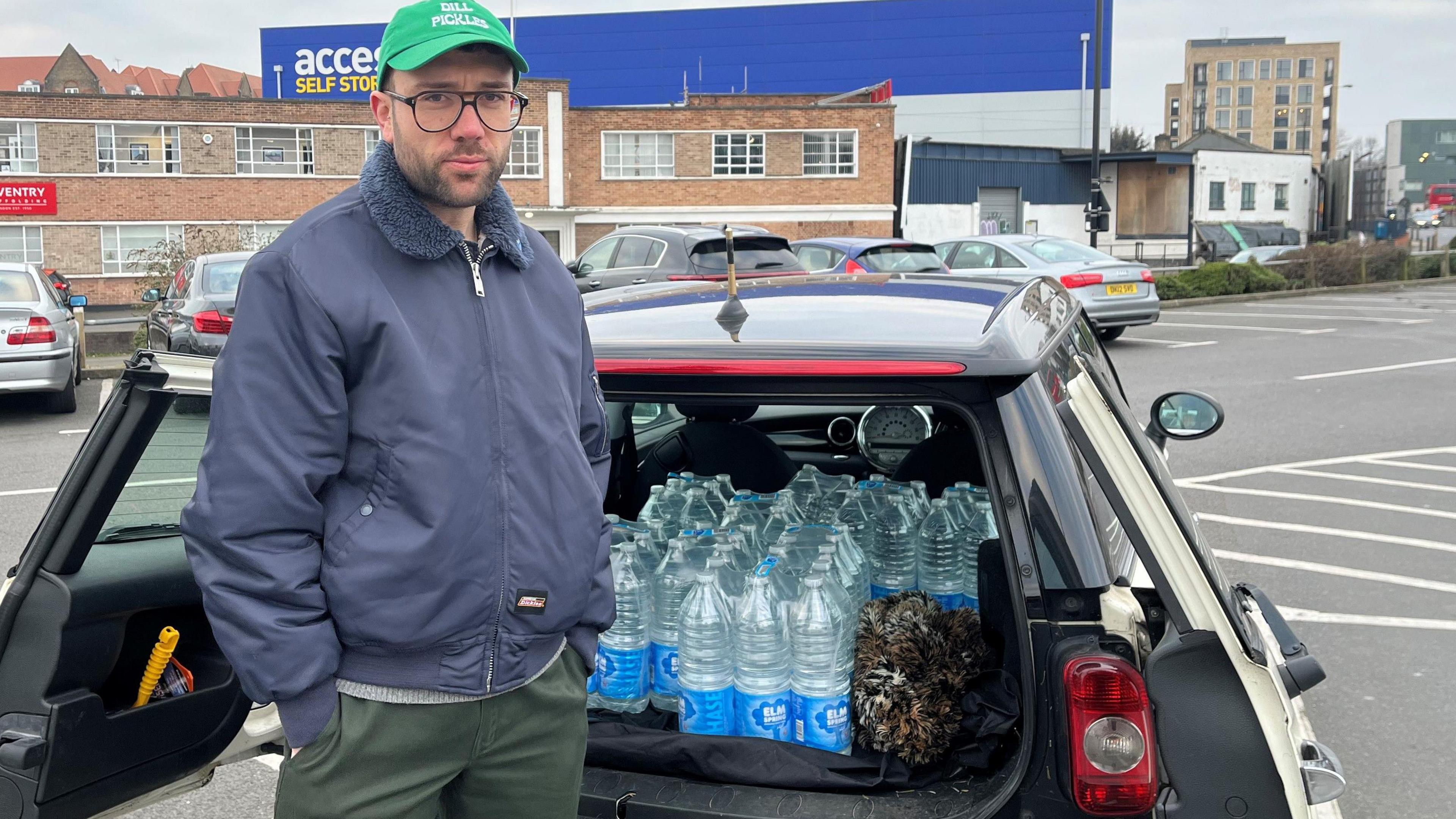 Christopher standing in front of his Mini car filled with bottles of water