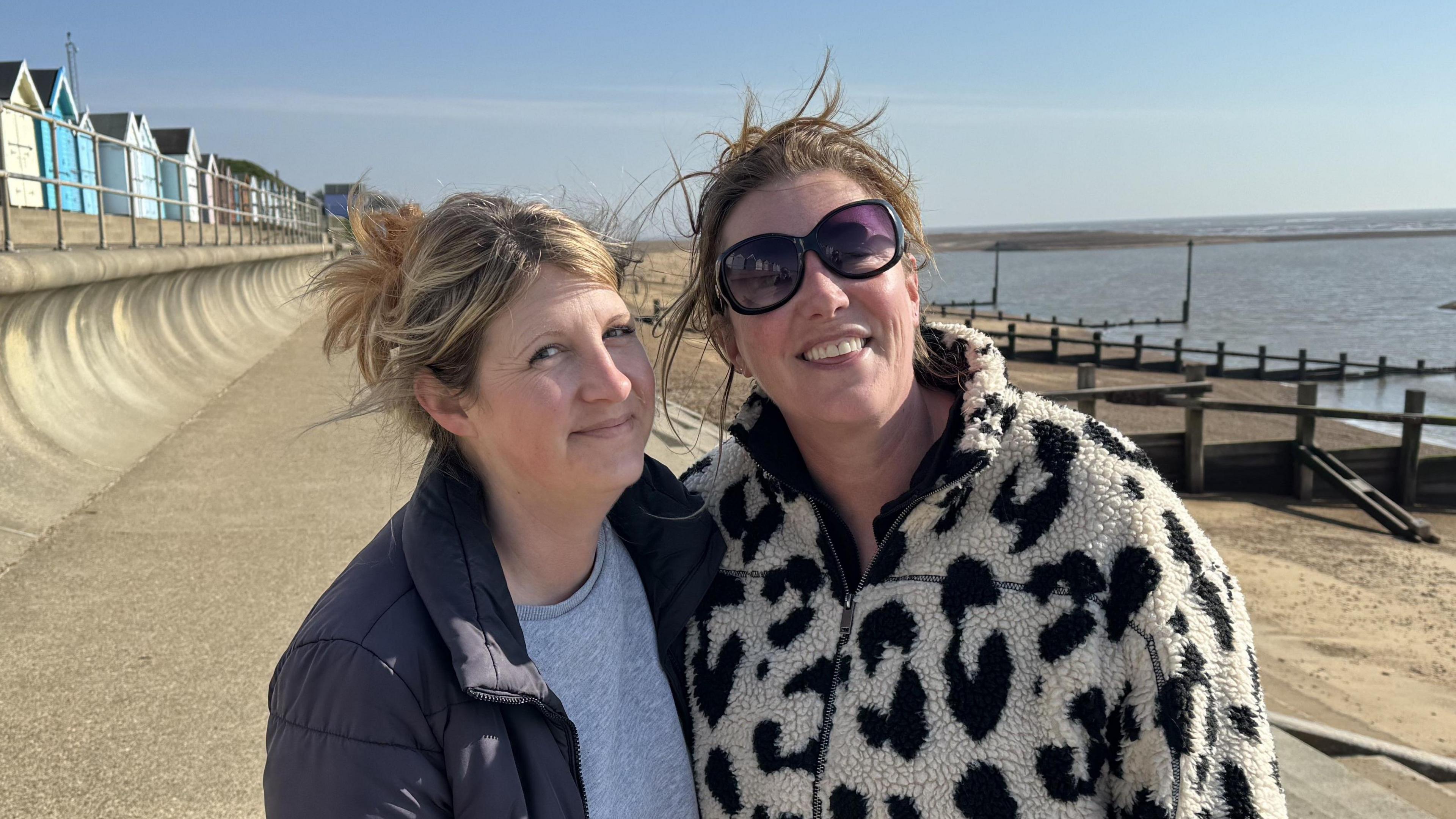 Imogen Ainsley and Jo Elliot standing side-by-side on the Felixstowe seafront. The beach and sea can be seen to the right, while beach huts can be seen in the background to the left.