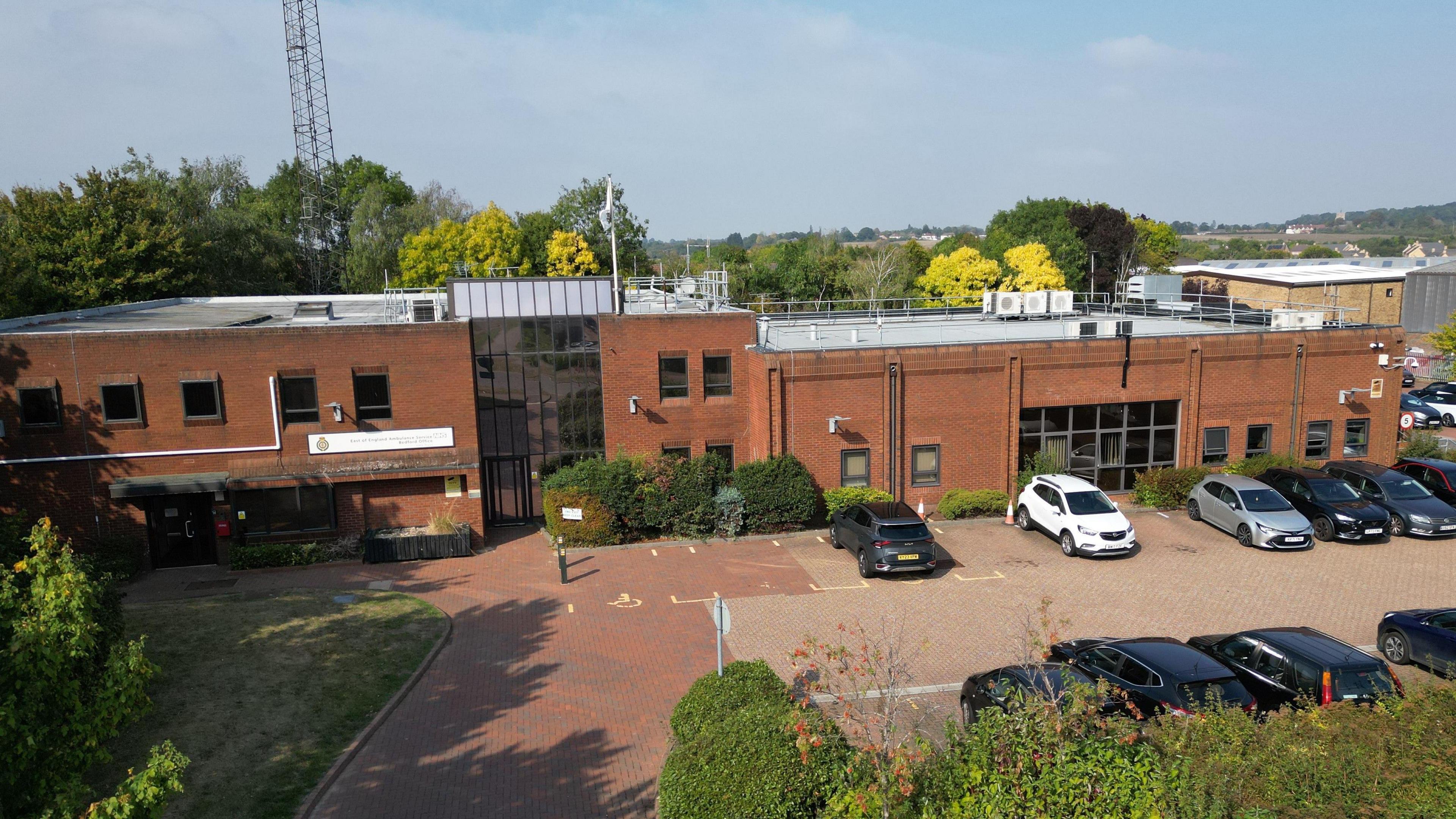 A drone image of the Bedford Emergency Operations Centre on Hammond Road. The red brick building is over two storeys and has several cars parked outside in a car park. 