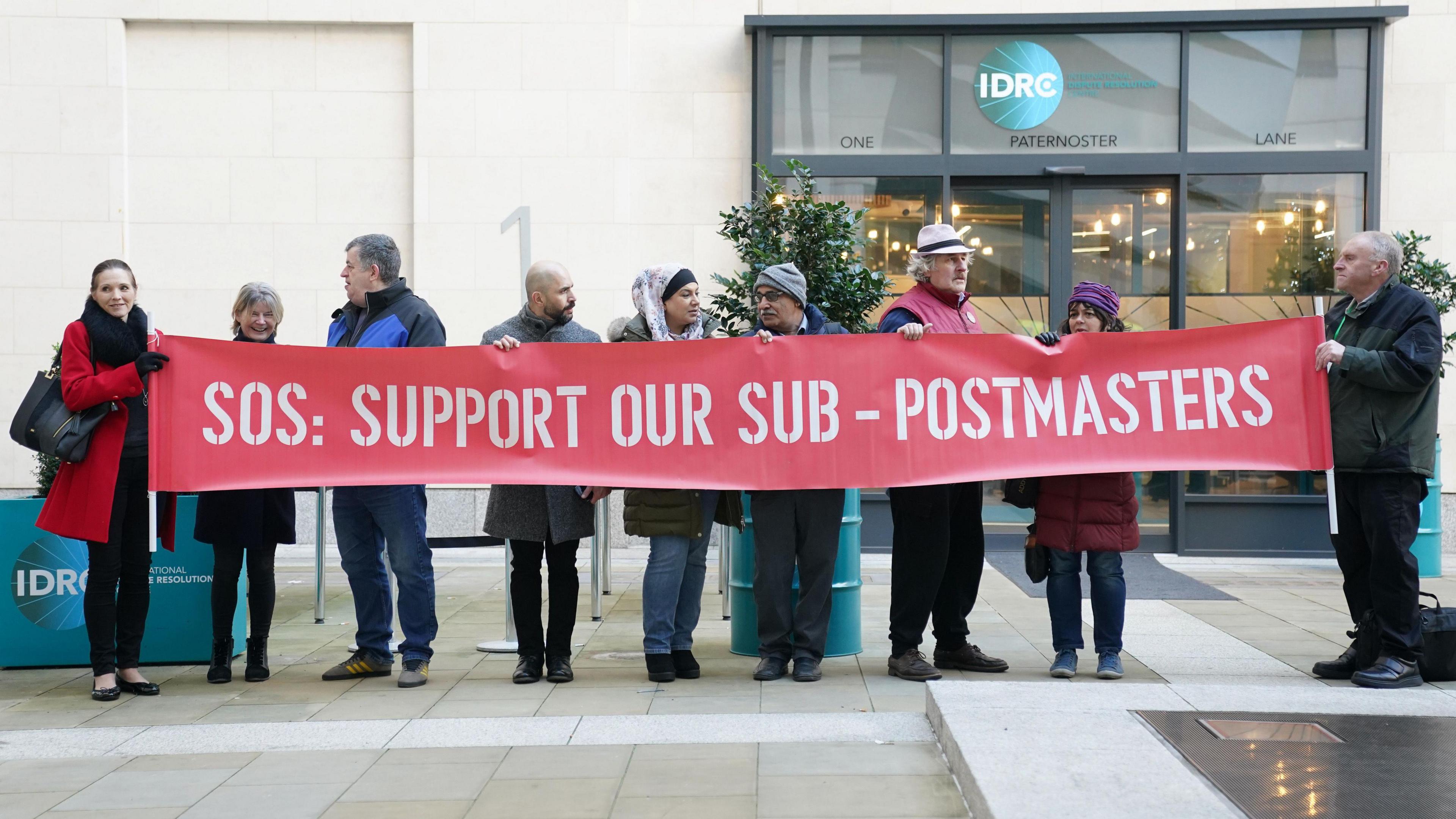 Nine campaigners holding a red banner which says SOS: Support our sub-postmasters