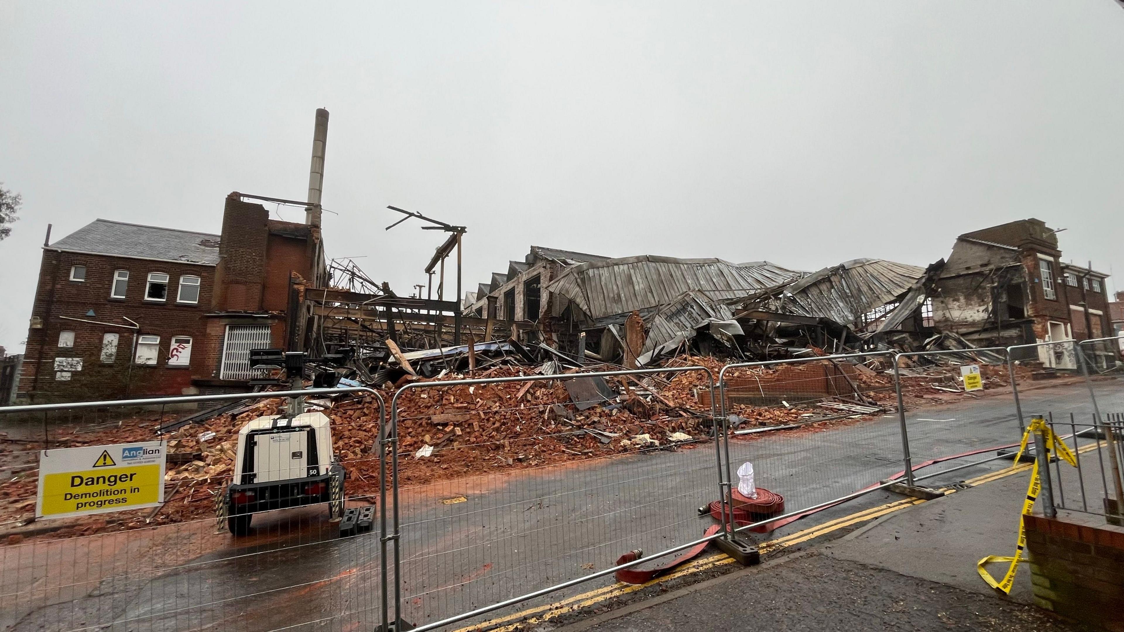 Large piles of rubble at the site of the former factory. Part of the roof has collapsed and the ruins can be seen in the background 