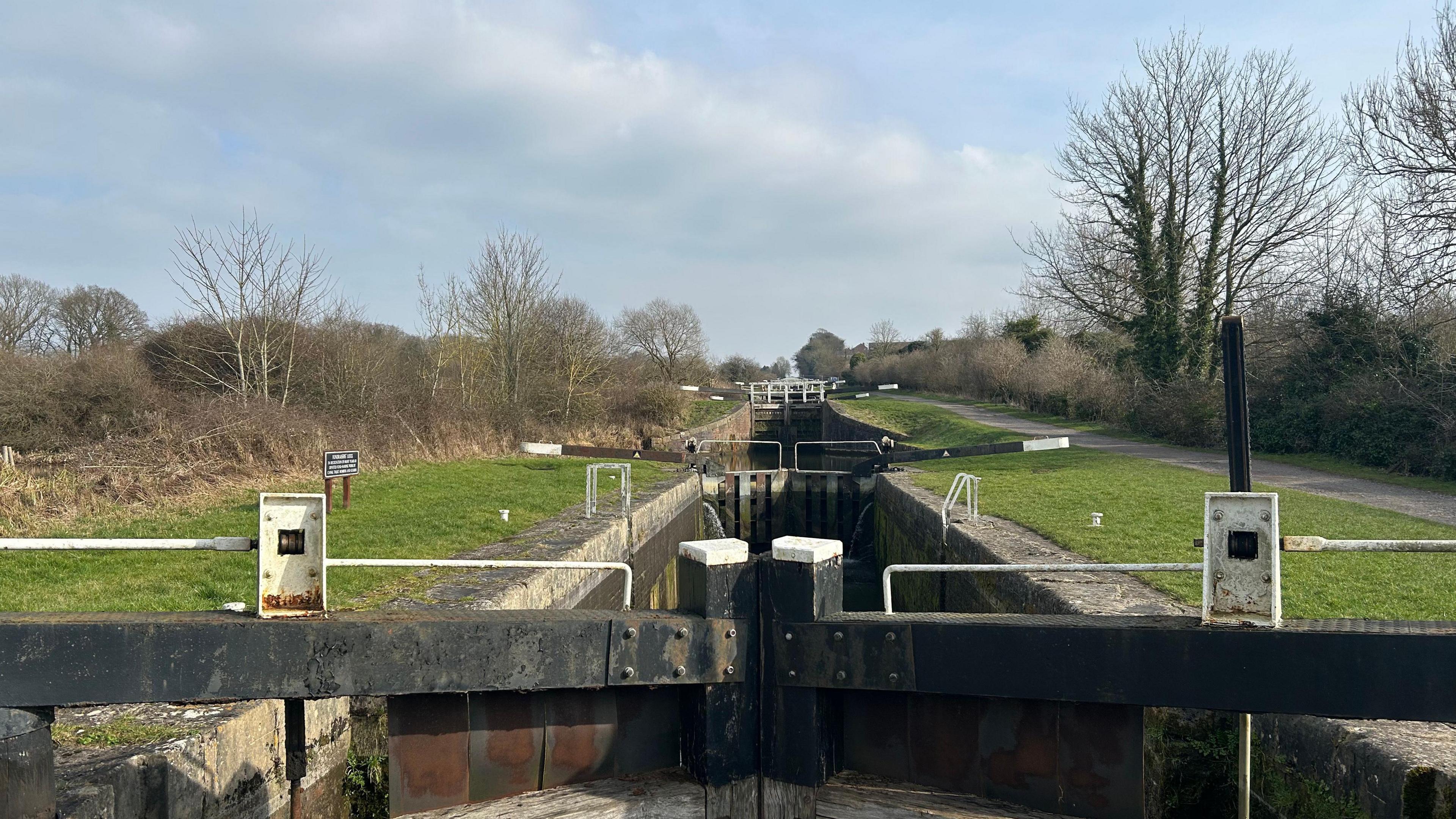 A canal and lock gates stretch into the distance with a canal, grass verges and trees on either side.