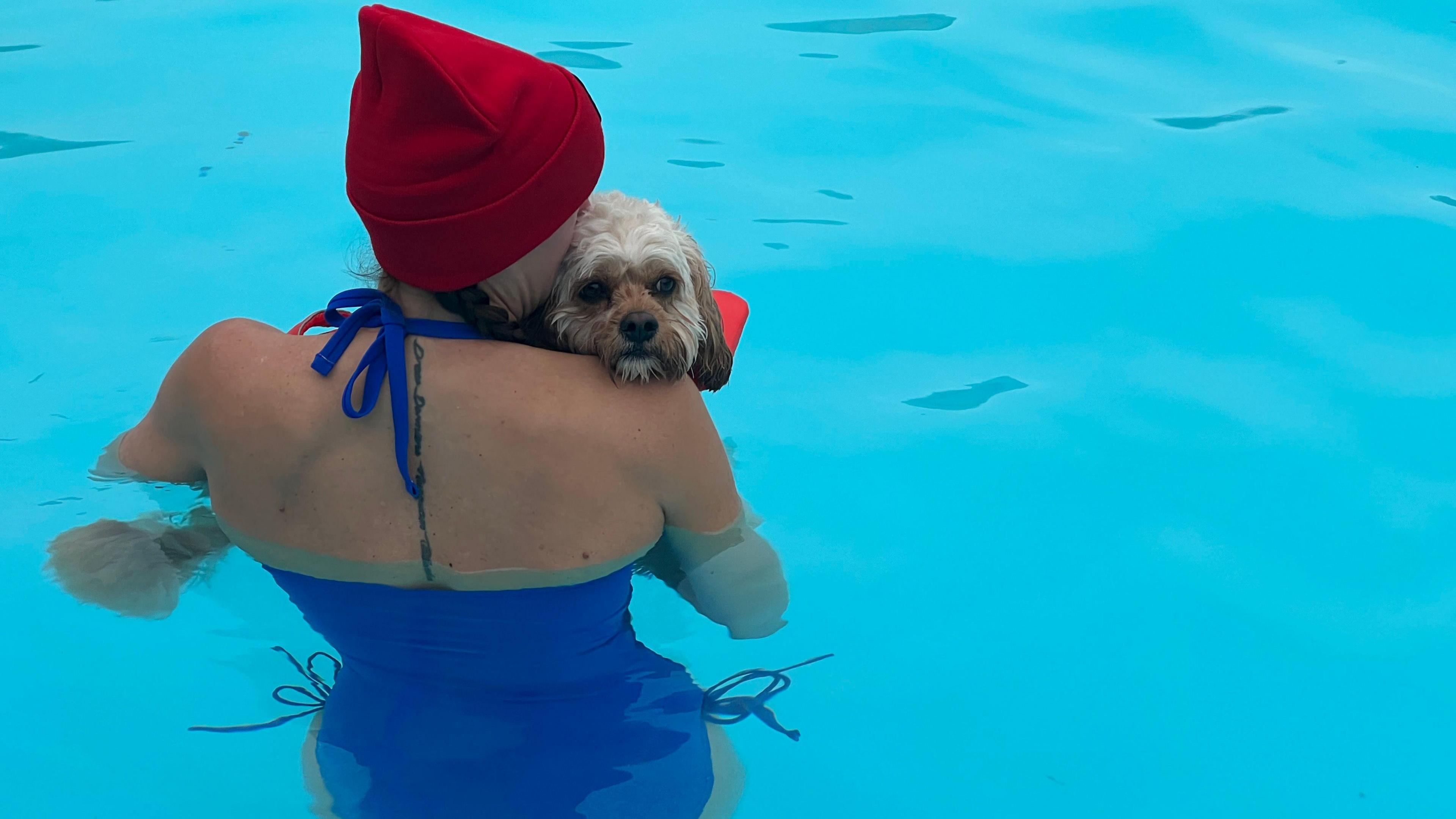 A woman in a blue swimsuit with a dog in her hands inside the water