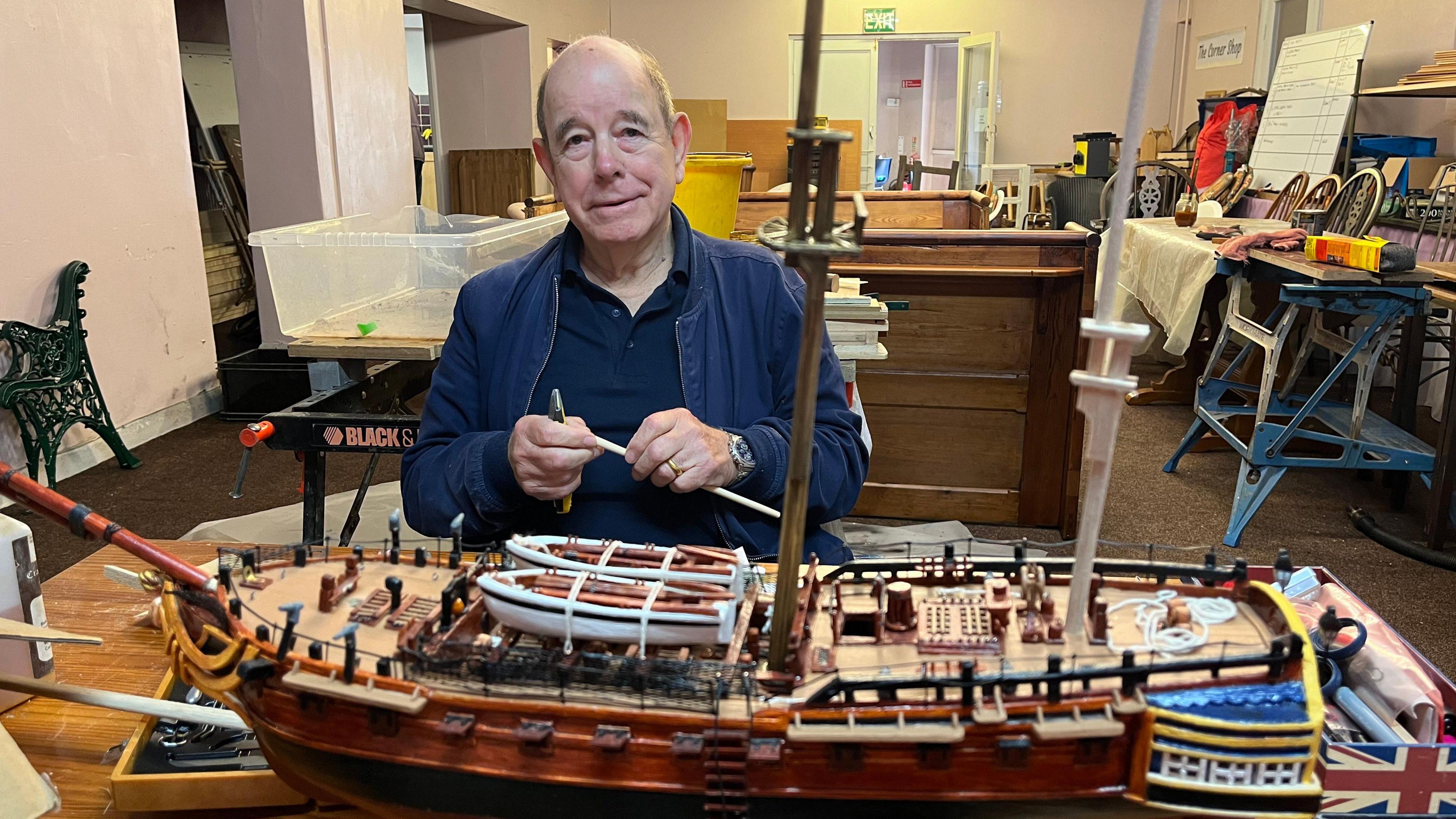 Bob Cooper standing behind a model ship that he is building