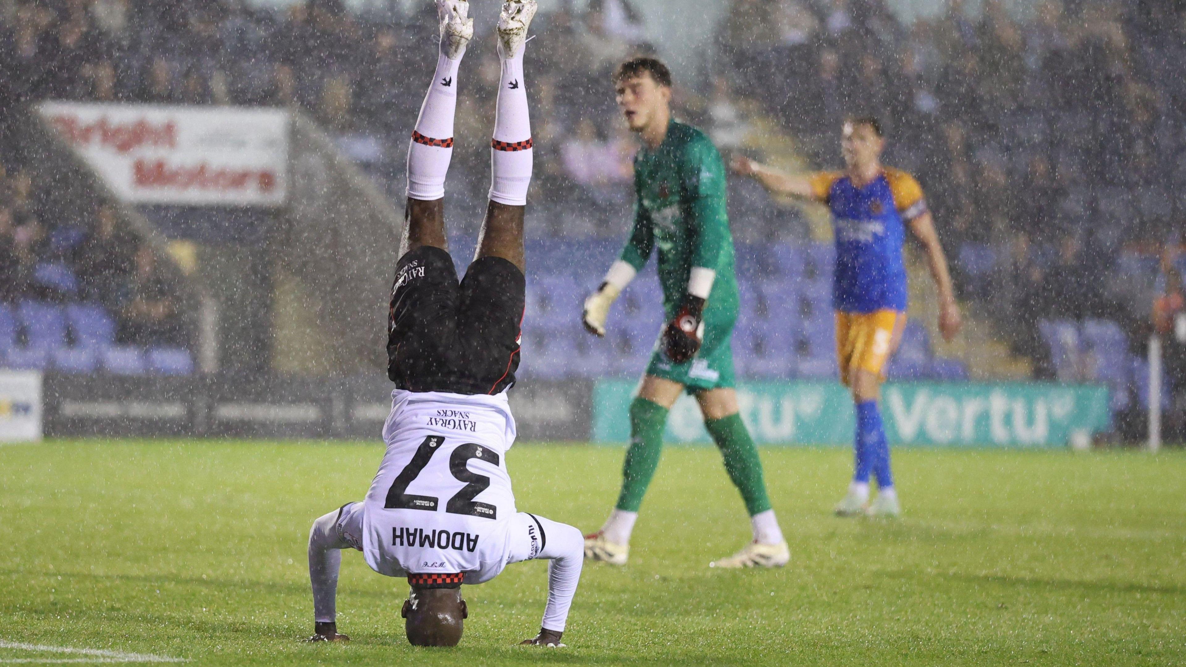 Albert Adomah doing his famous 'headstand' celebration in the rain at Shrewsbury Town last night, literally standing on his head with his legs straight, wearing the club's away white and black kit
