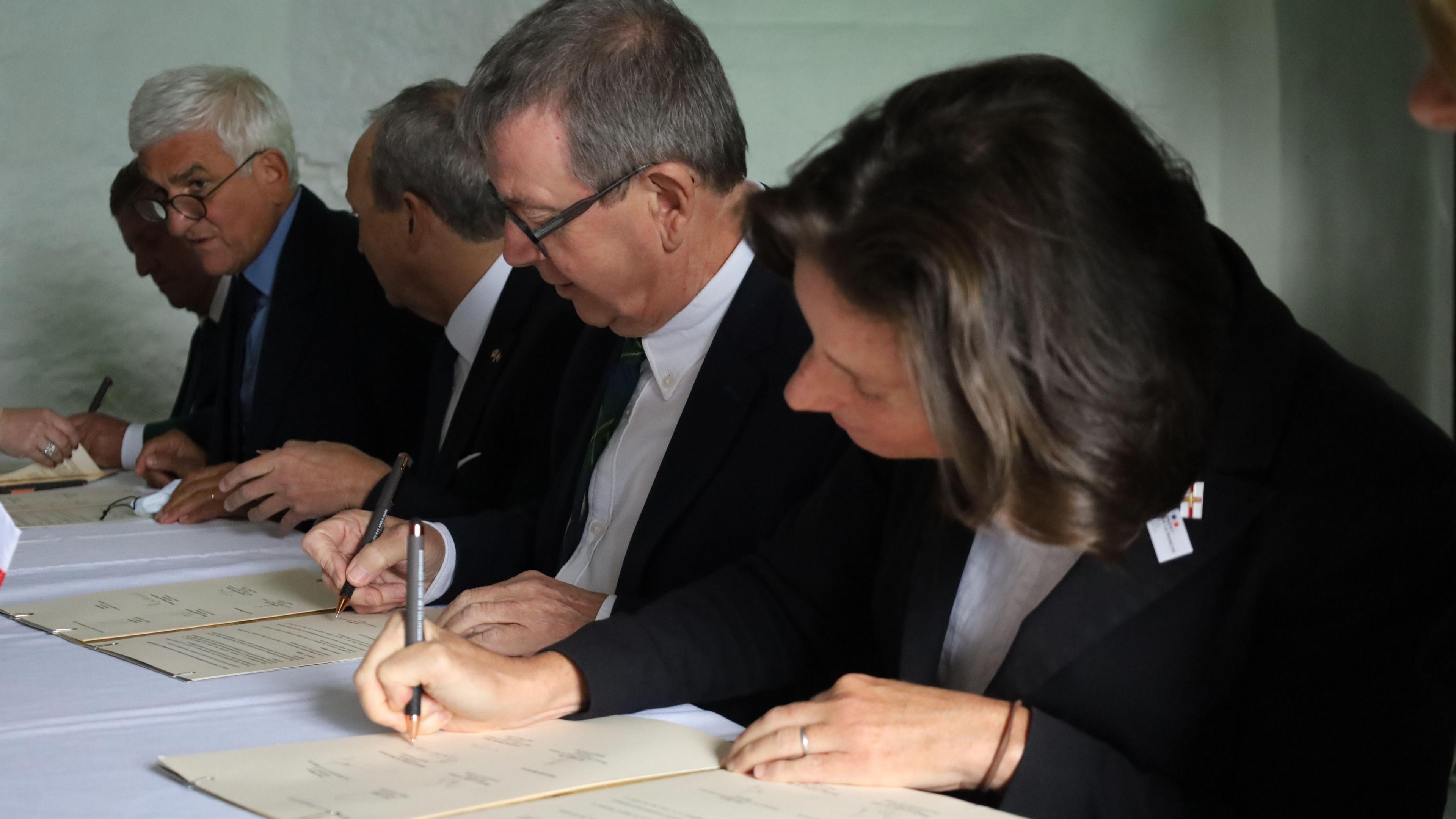 A woman and three men sit at a table signing documents.