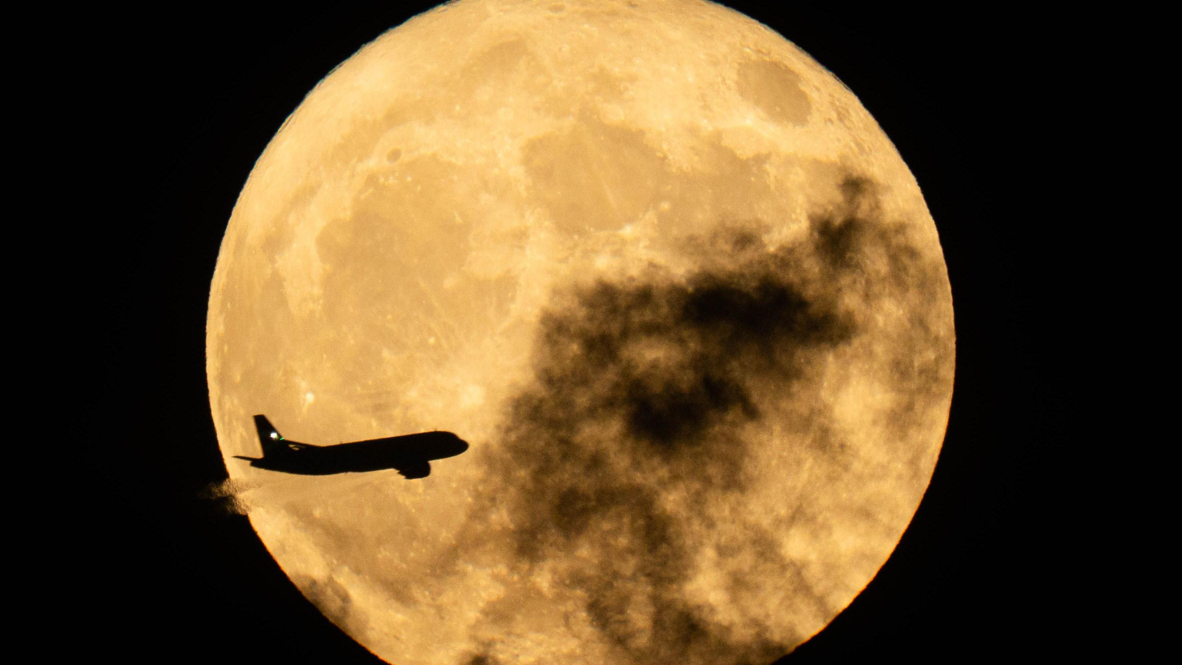 A plane seen flying in front of a Flower Moon