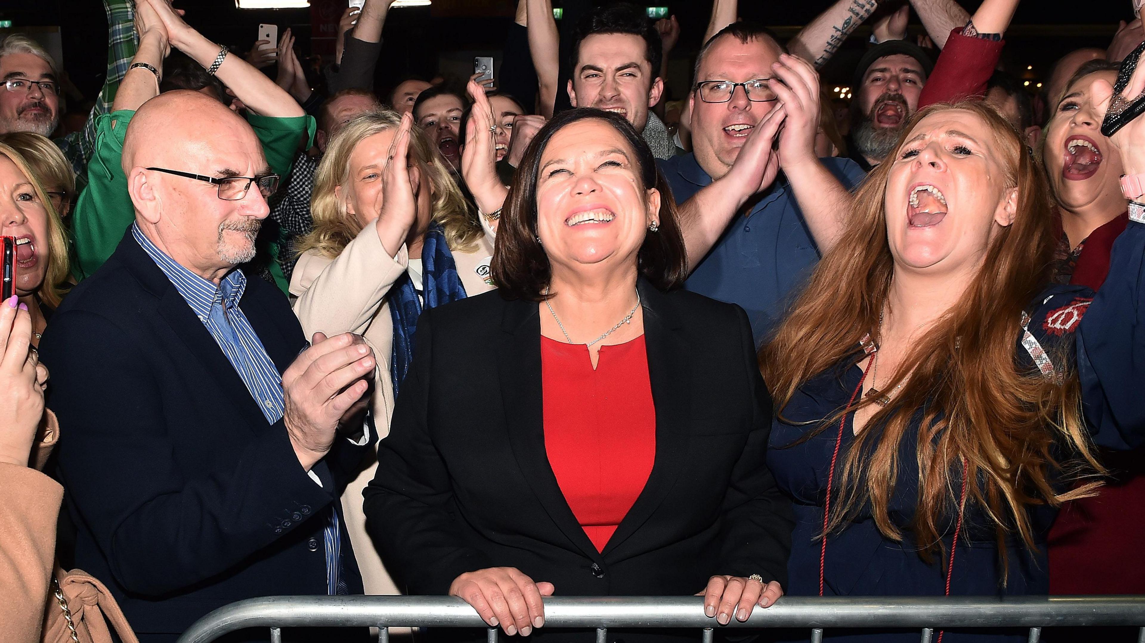 Mary Lou McDonald celebrates with her supporters after being elected at the RDS Count centre in 2020. She has a wide smile and she's surrounded by people cheering and clapping.