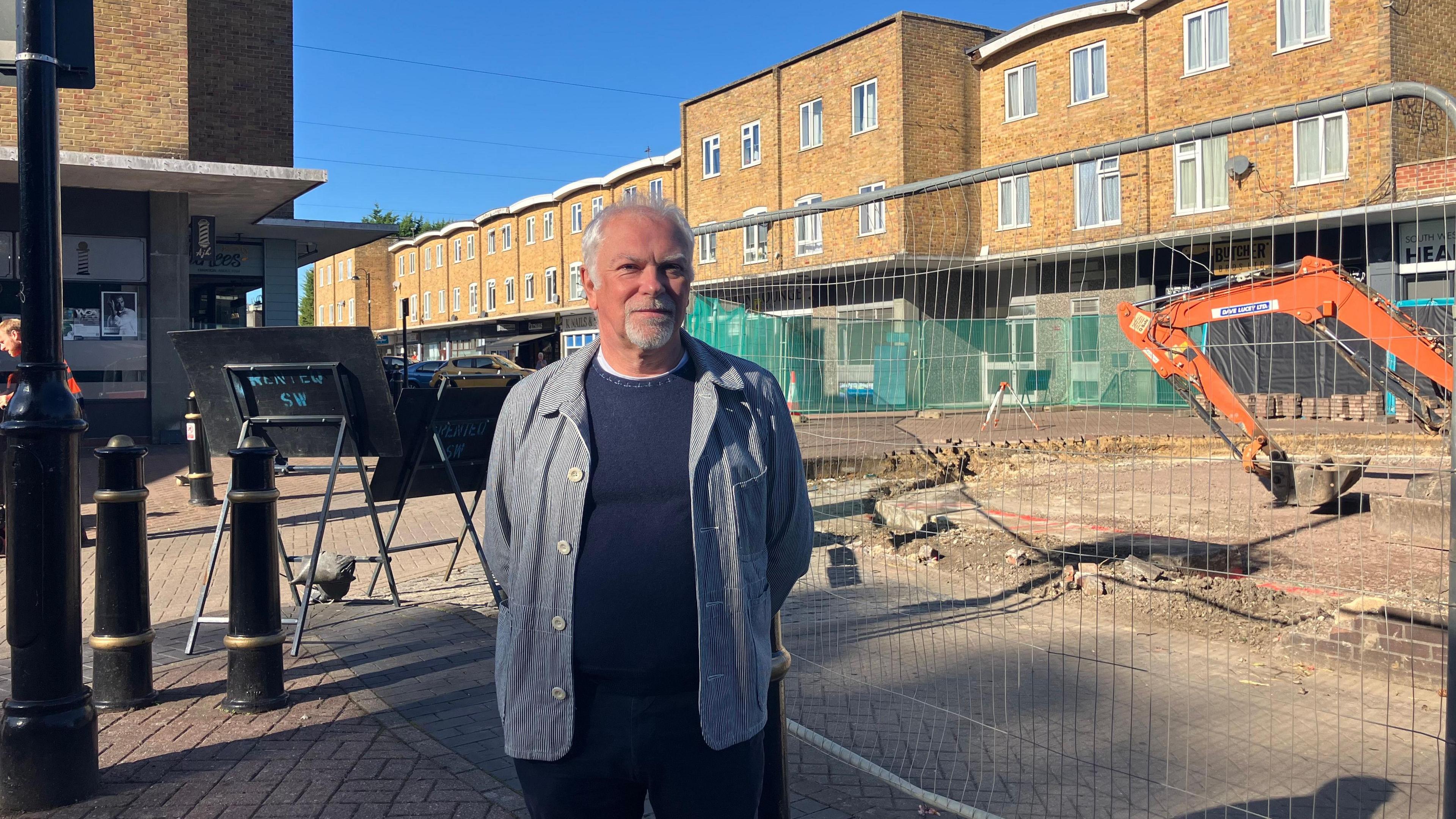 Mark Bailey, of Westbury Town Council, stood next to a construction site for the new rotunda in Devizes. There is an orange digger and a high fence next to him.