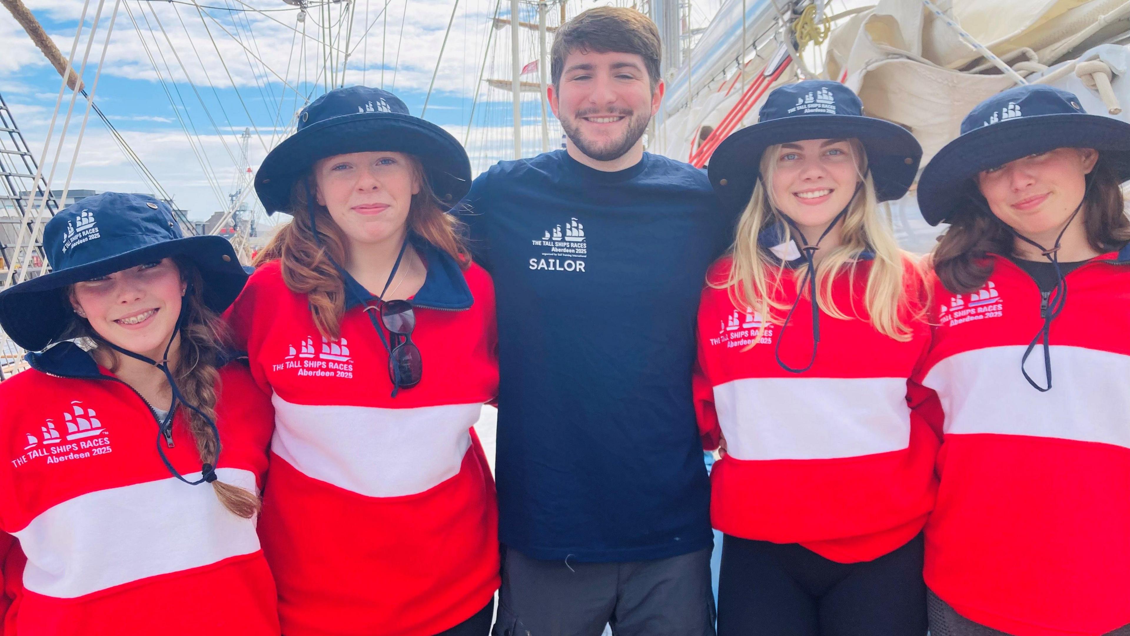 Teenagers Mya, Katherine, Freya and Mia with mentor Toby on their tall ship, smiling at the camera.