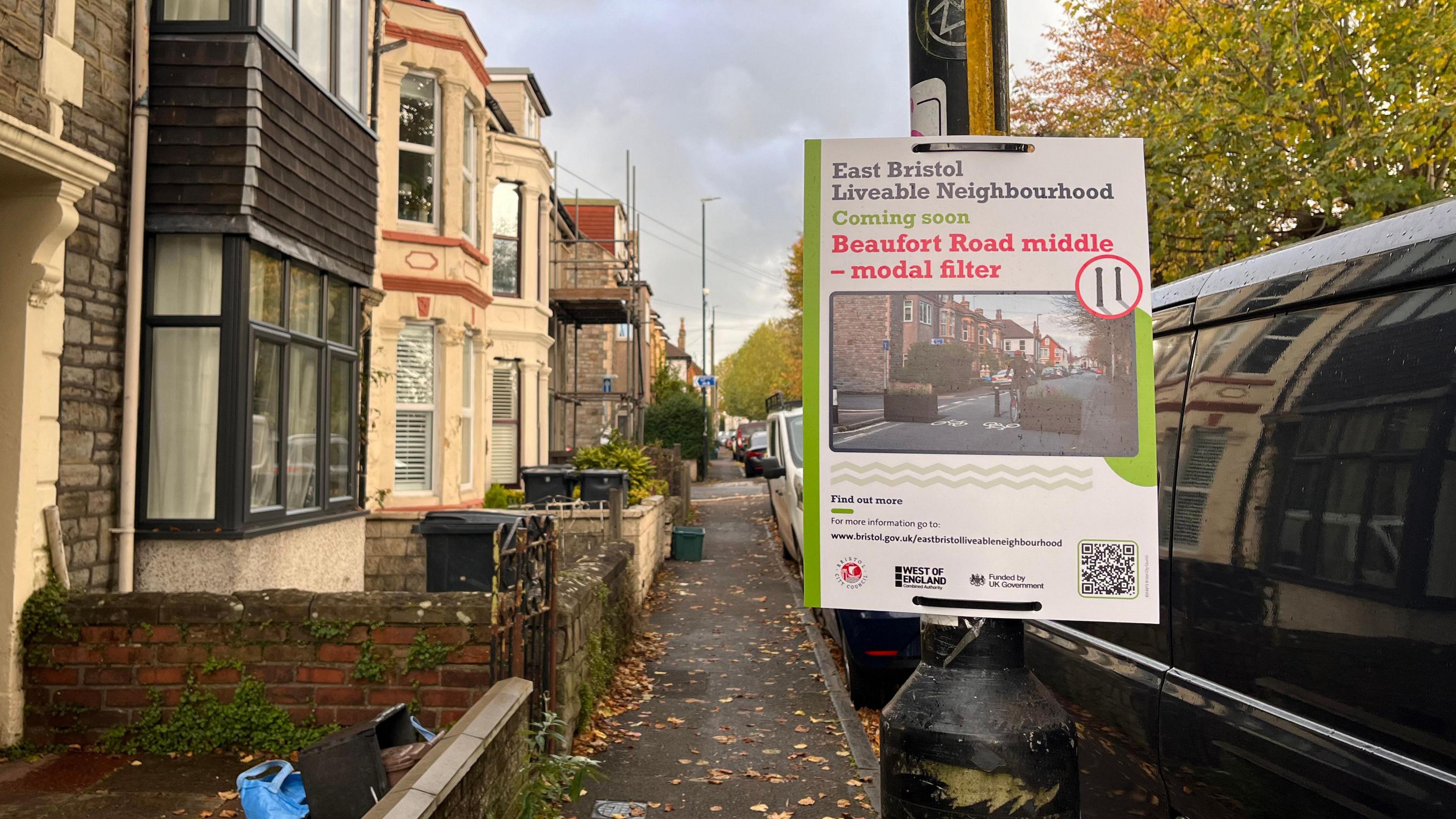 A sign about the East Bristol Liveable Neighbourhood project tied to a lampost on a street dotted with leaves