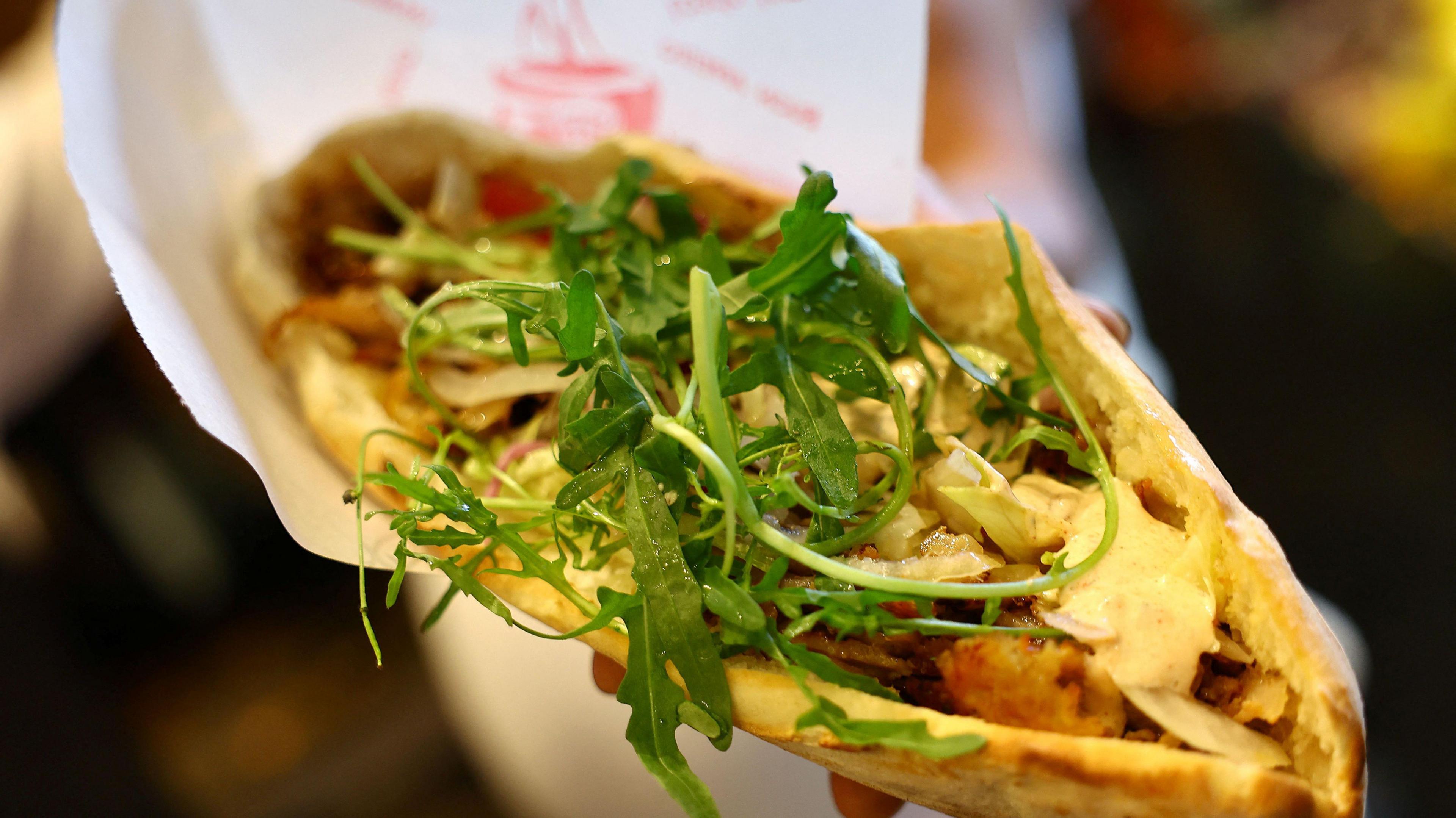 A doner is being held towards the camera. It has rocket on top of it and is wrapped in paper.