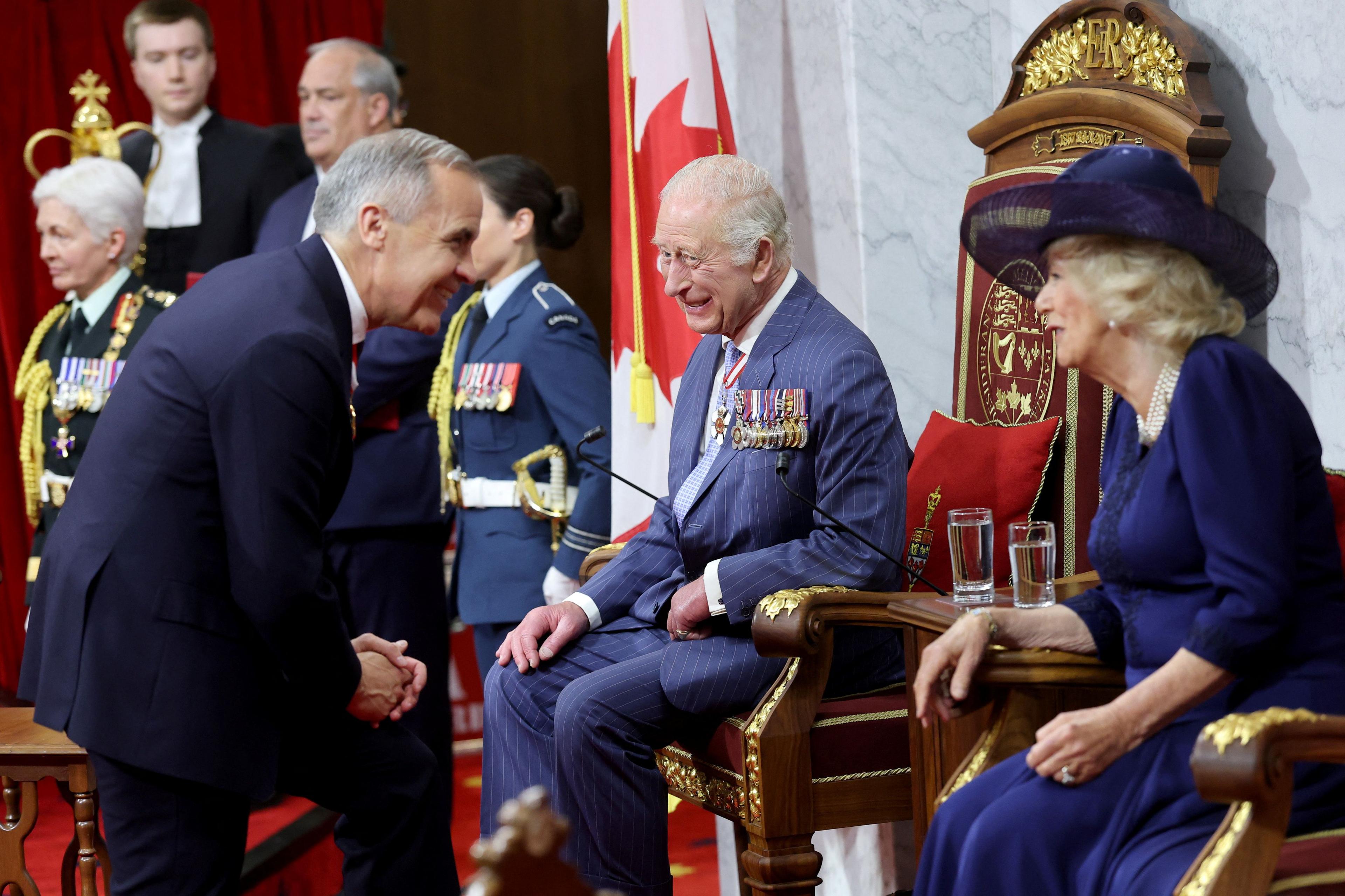 Mark Carney bends down to King Charles and Queen Camilla who sit on thrones.