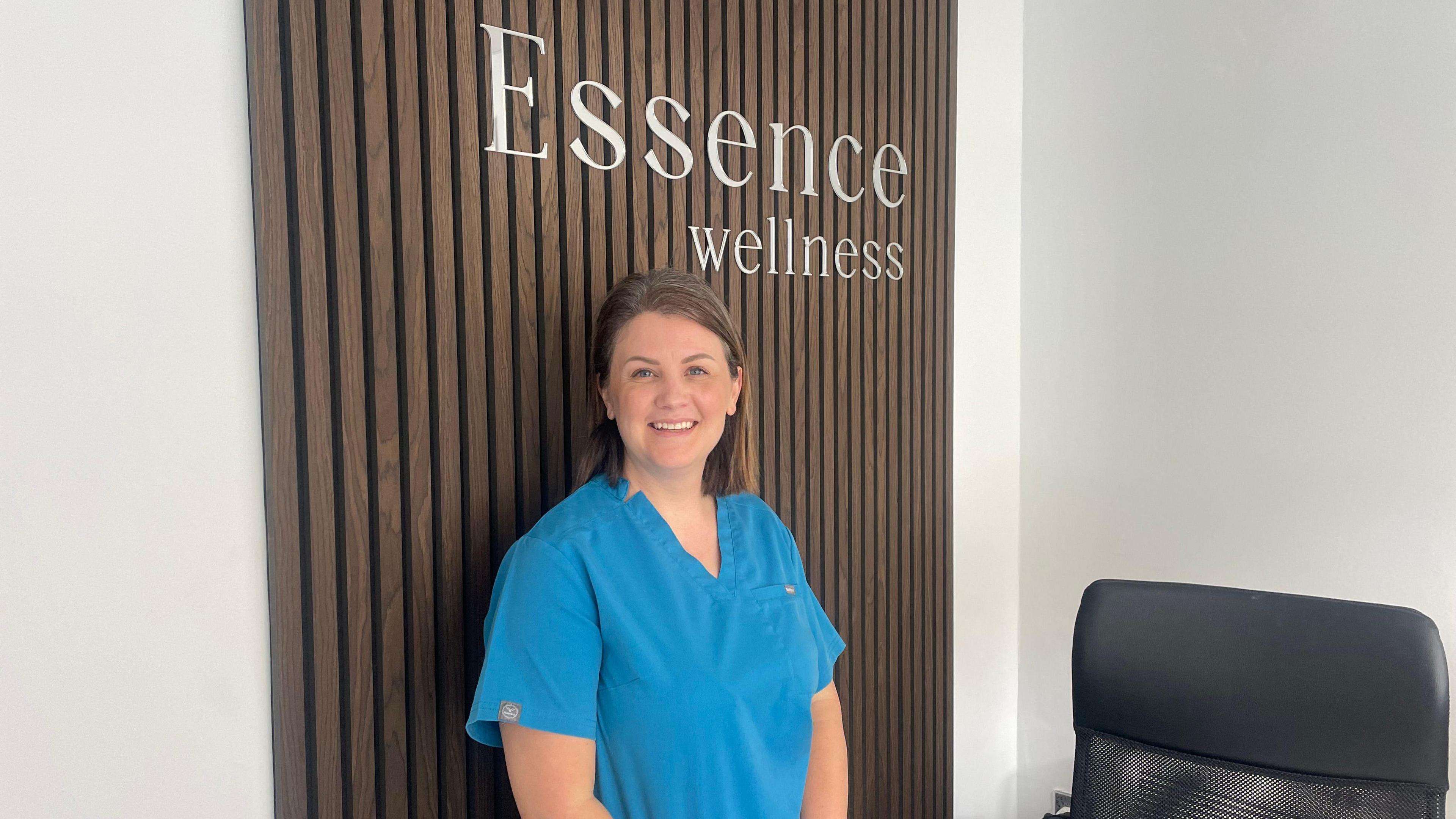 Owner of business in blue scrubs in front of 'Essence Wellness' sign