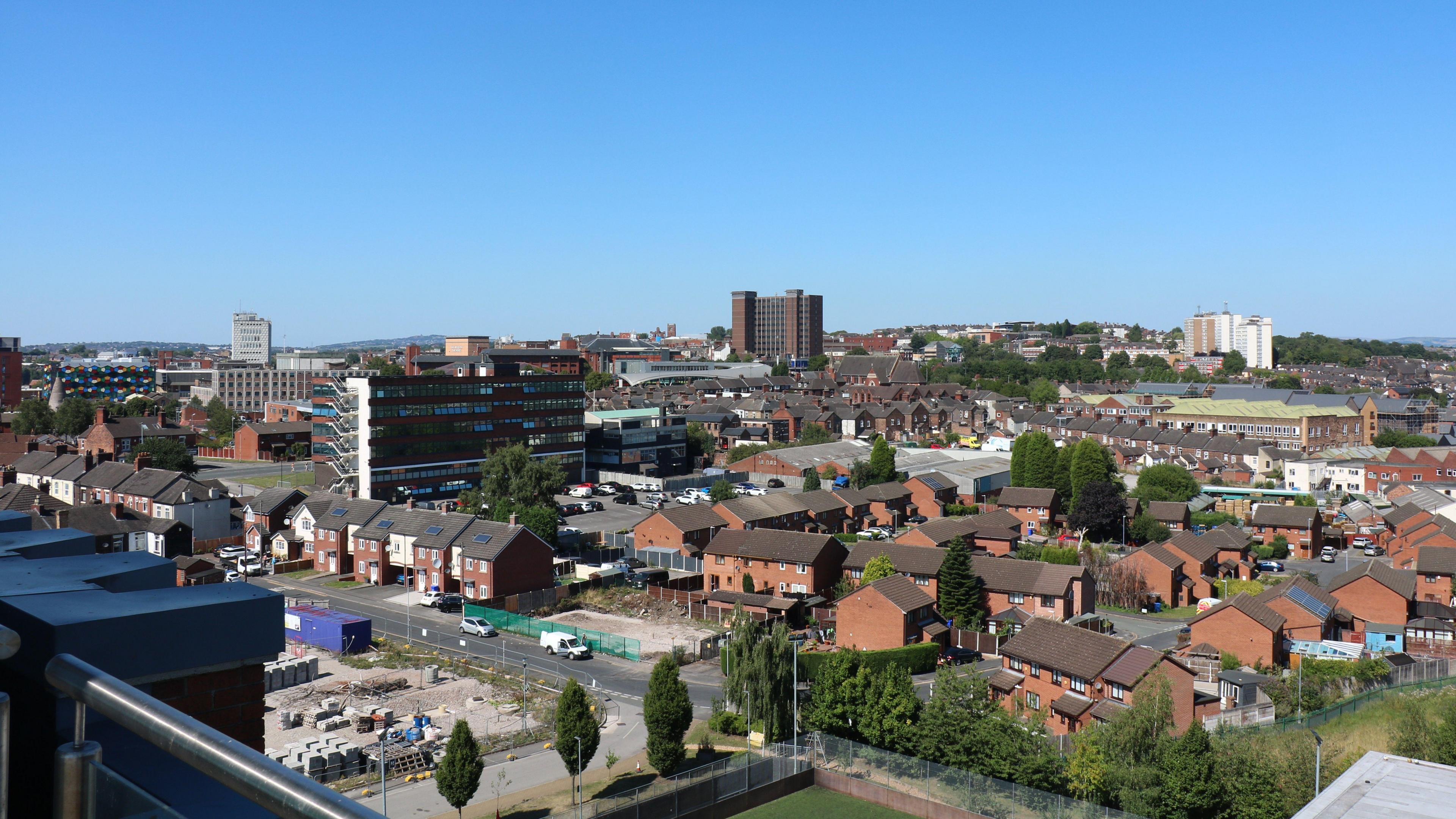 A city centre skyscape with a blue sky, four tall buildings rise up above a series of smaller two-storey houses