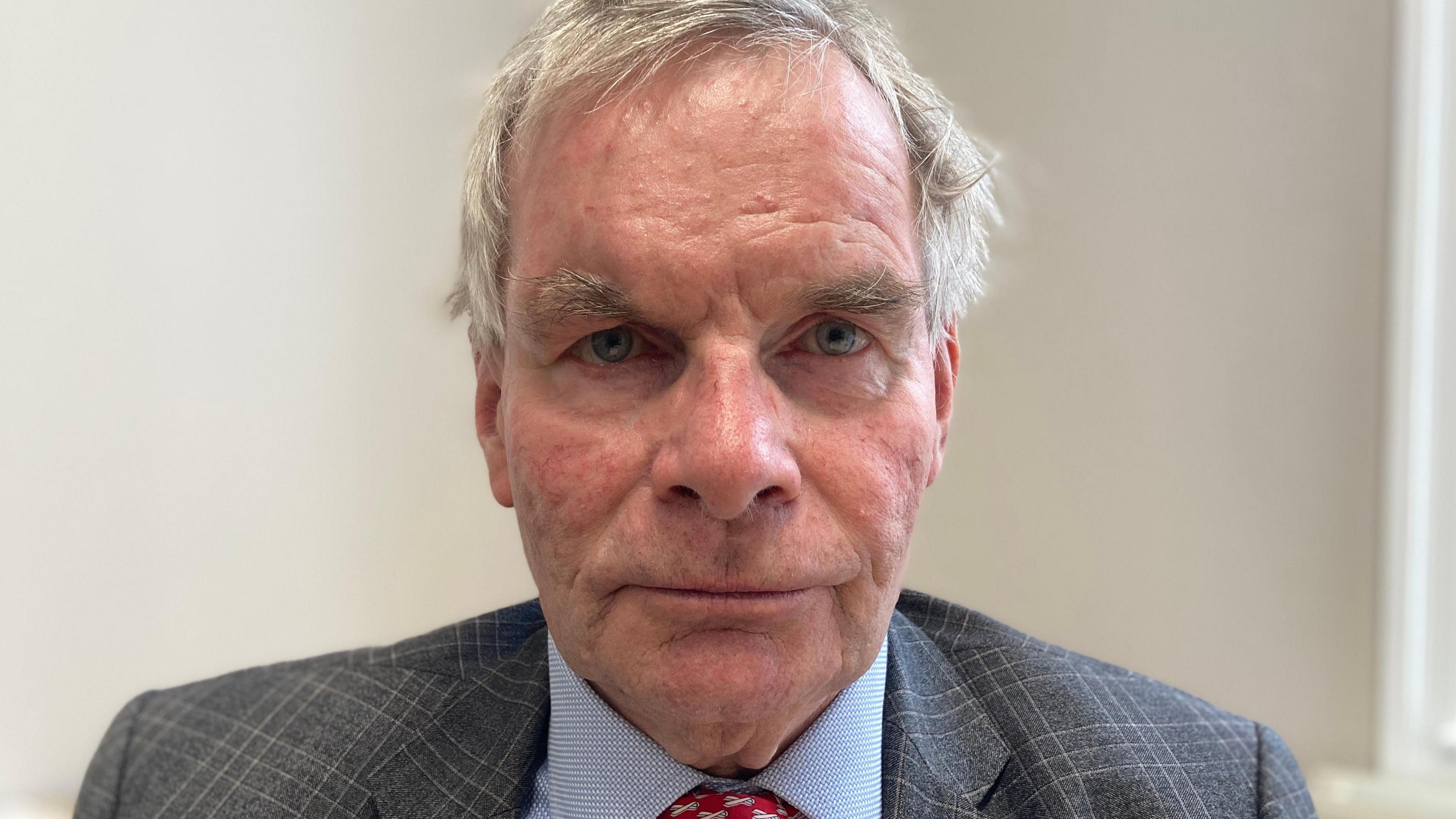 Head and shoulders shot of Martin Hill looking into the camera. He has grey hair and is wearing a blue shirt, red tie and grey suit jacket 