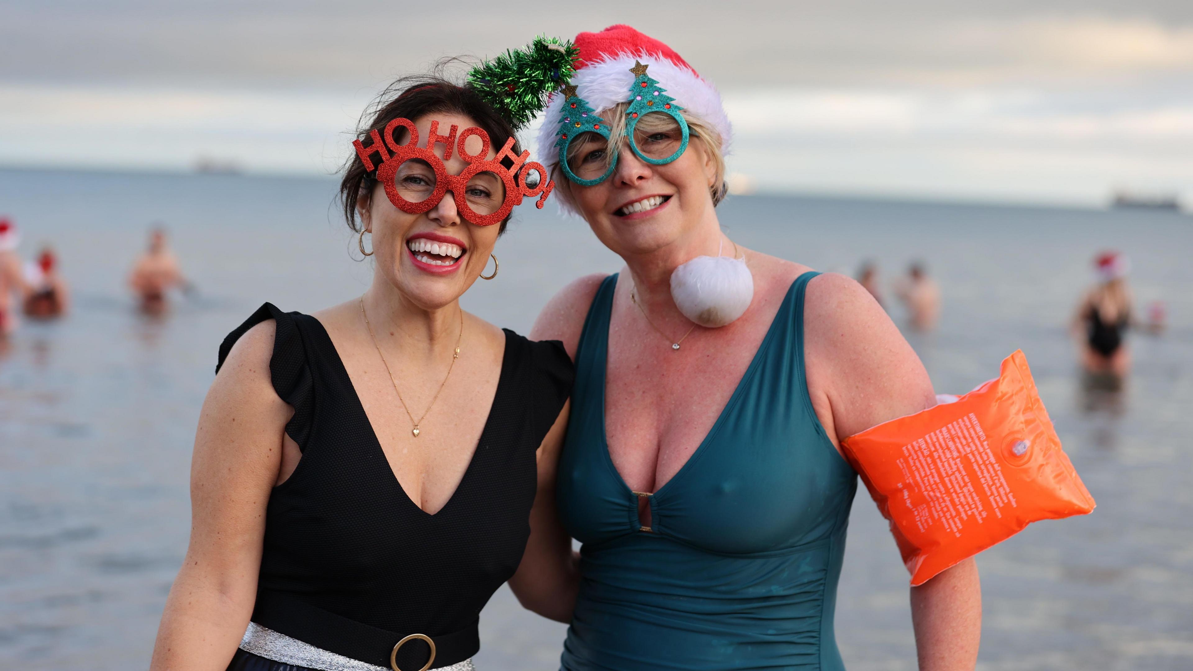 Nicola McIlhagger (left) and Patricia McKelvey. Nicola is wearing a black swimsuit. She has dark hair and is wearing red novelty glasses with the words "HO HO HO" on them. Patricia is wearing a teal swimsuit and a santa hat and orange inflatable armband. Her novelty glasses feature Christmas trees.