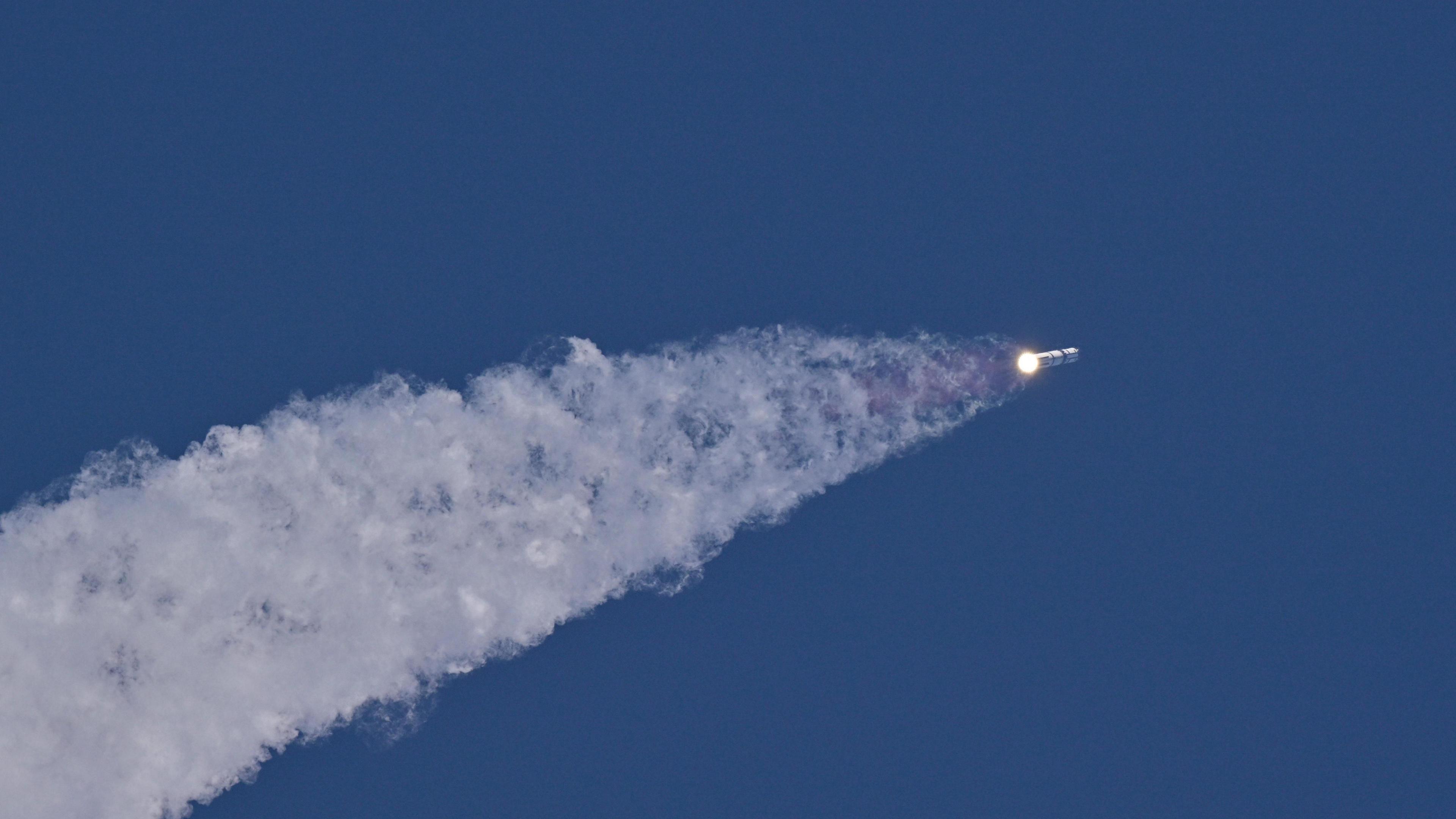 A SpaceX Super Heavy booster carrying the Starship spacecraft flies into the sky leaving behind a trail