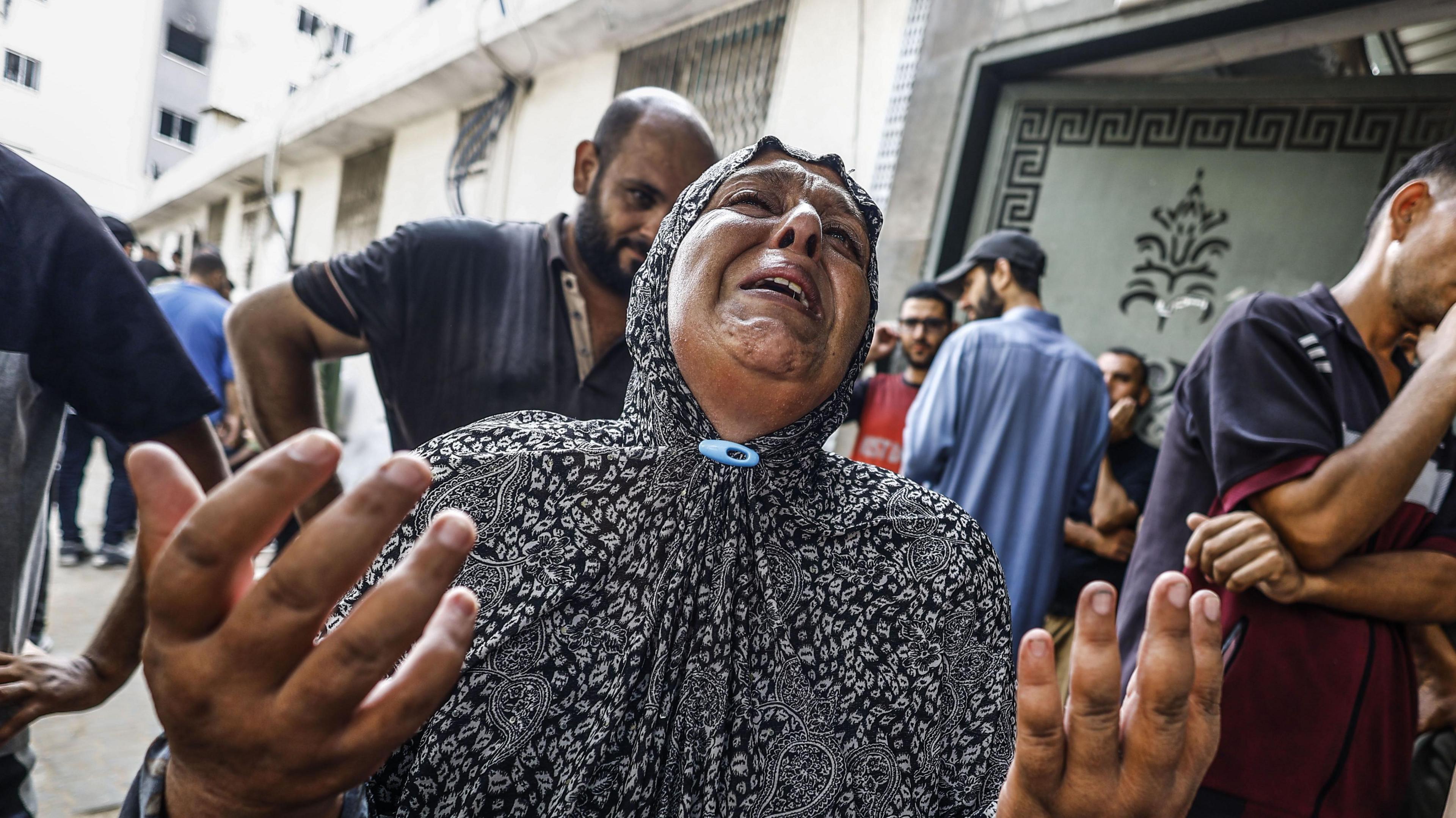 A woman wearing a dark robe crying with lots of other people behind her at al-Shifa Hospital