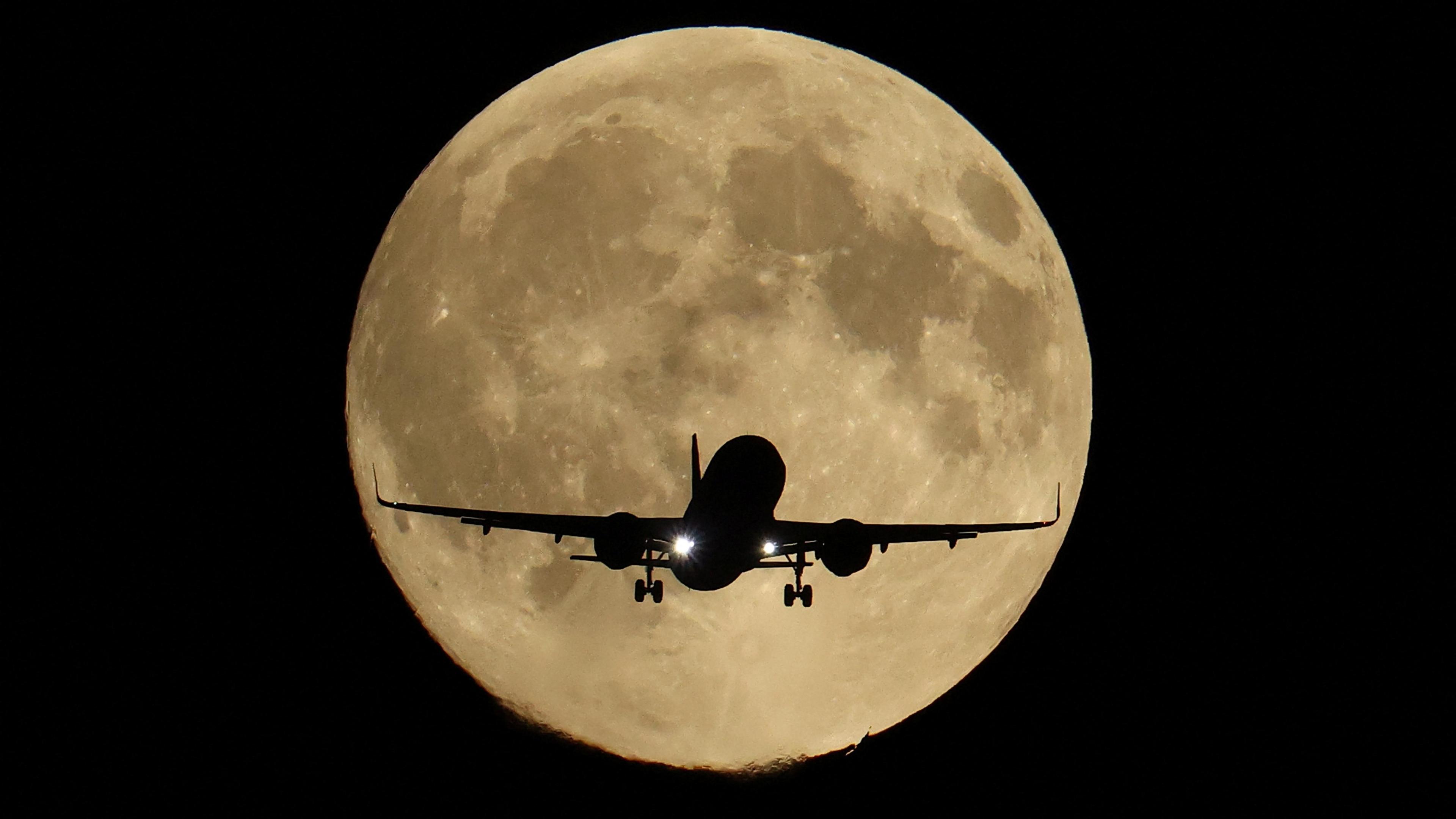 A flying passenger plan is dwarfed by a sepia-tinged brilliant supermoon 