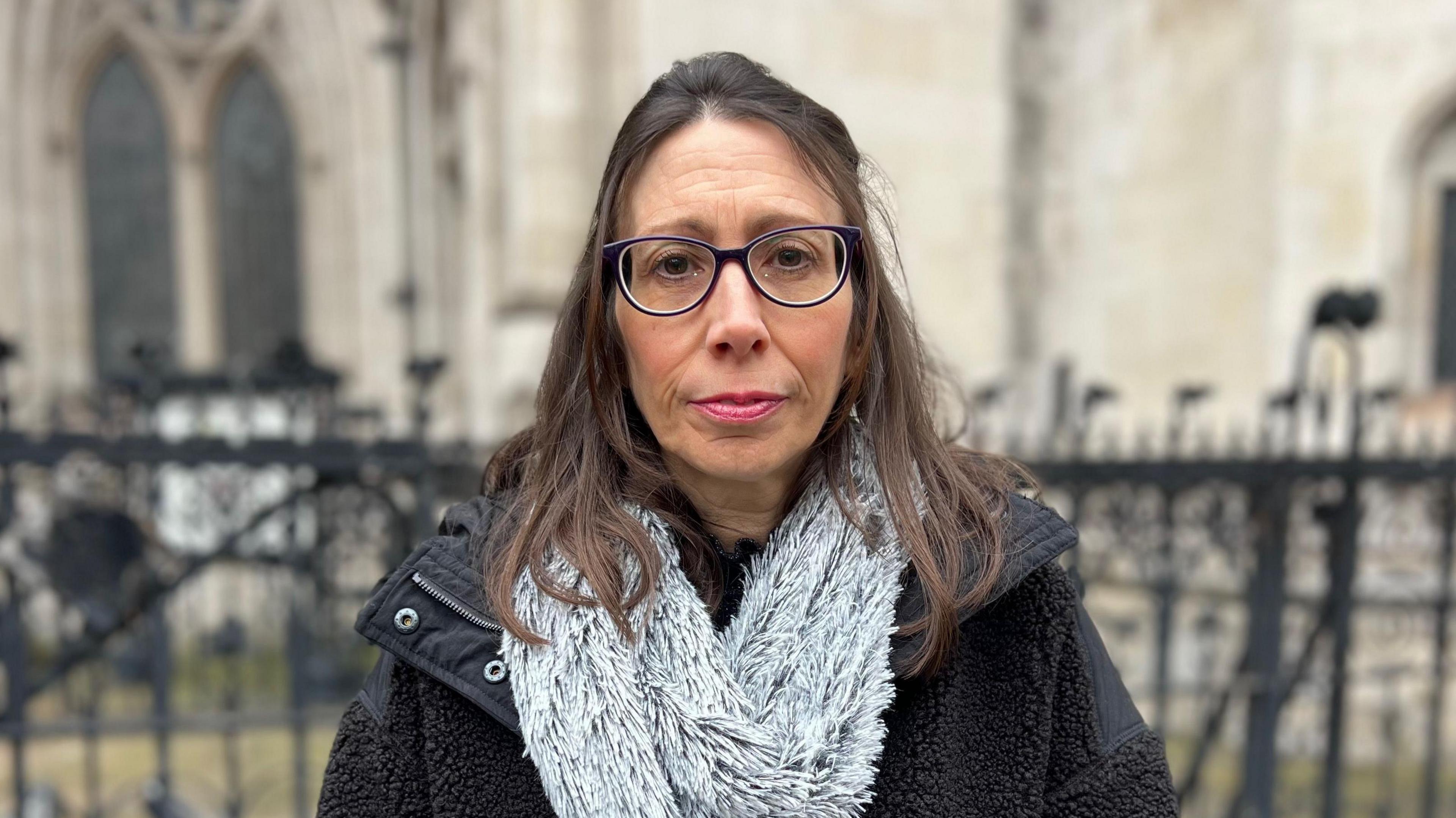 Kristie Higgs, pictured outside the Court of Appeal. She has shoulder-length brown hair, and wears dark glasses and pink lipstick. She is also wearing a dark winter coat and a fluffy grey scarf, and is looking directly at the camera. 